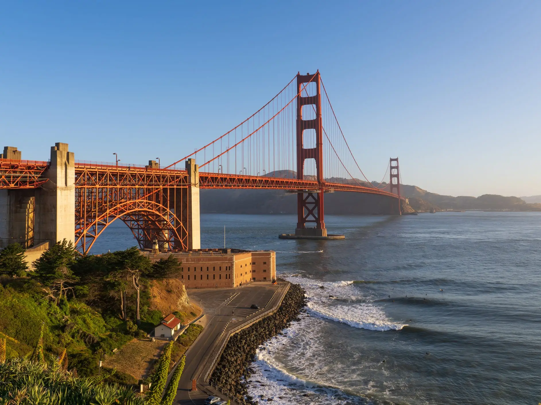 Golden Gate Bridge spans the bay above a coastal road and surf under a clear blue sky.