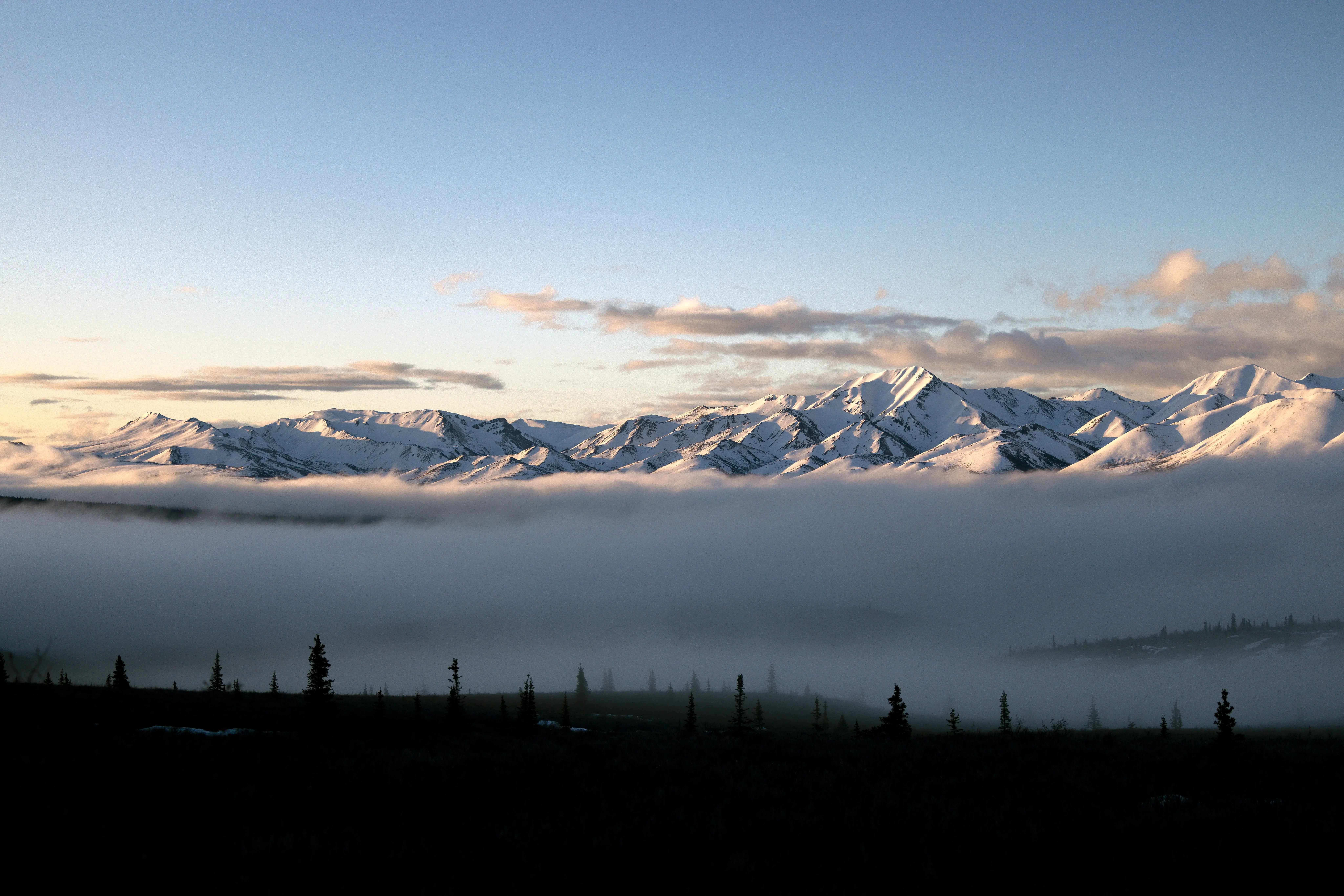 Clouds hover below snow-capped mountains.