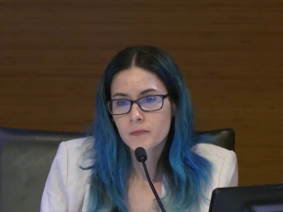 The writer sitting at a black chair and in front of a microphone during a City Council meeting.
