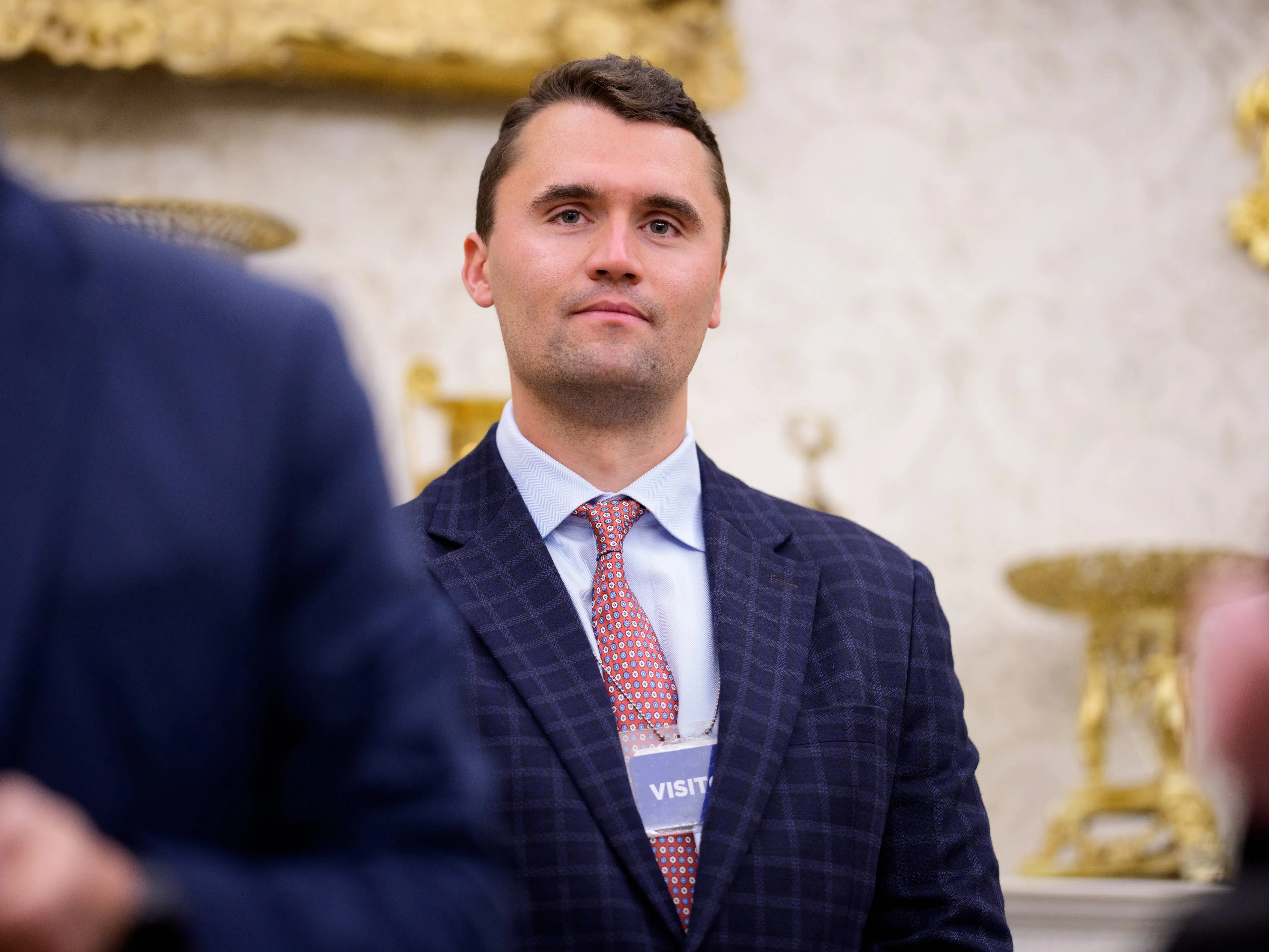 Turning Point USA co-founder Charlie Kirk stands in the back of the room as U.S. President Donald Trump speaks during a swearing in ceremony for interim U.S. Attorney for Washington, D.C. Jeanine Pirro in the Oval Office of the White House on May 28, 2025 in Washington, DC.