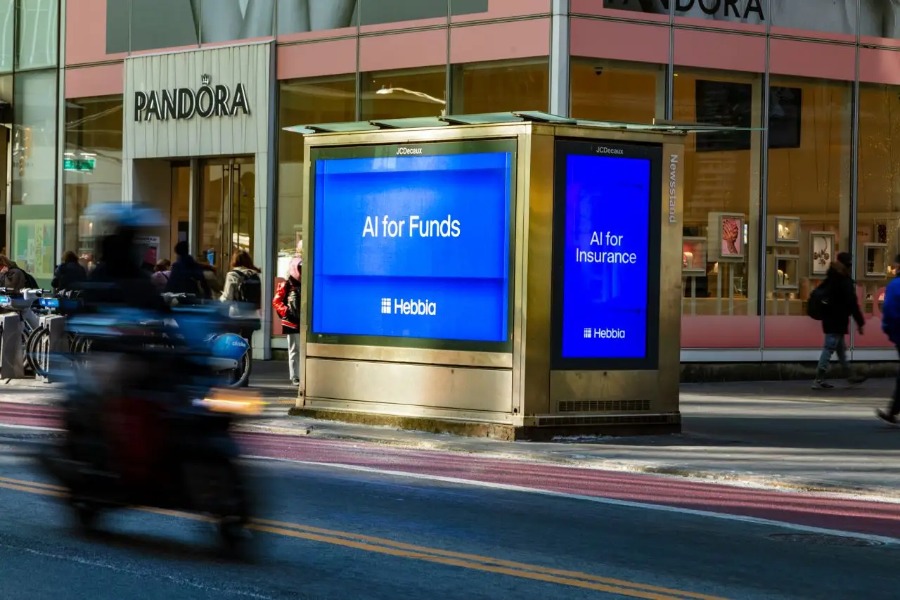 Street scene with digital ads for Hebbia, pedestrians, and a blurred motorcycle passing.
