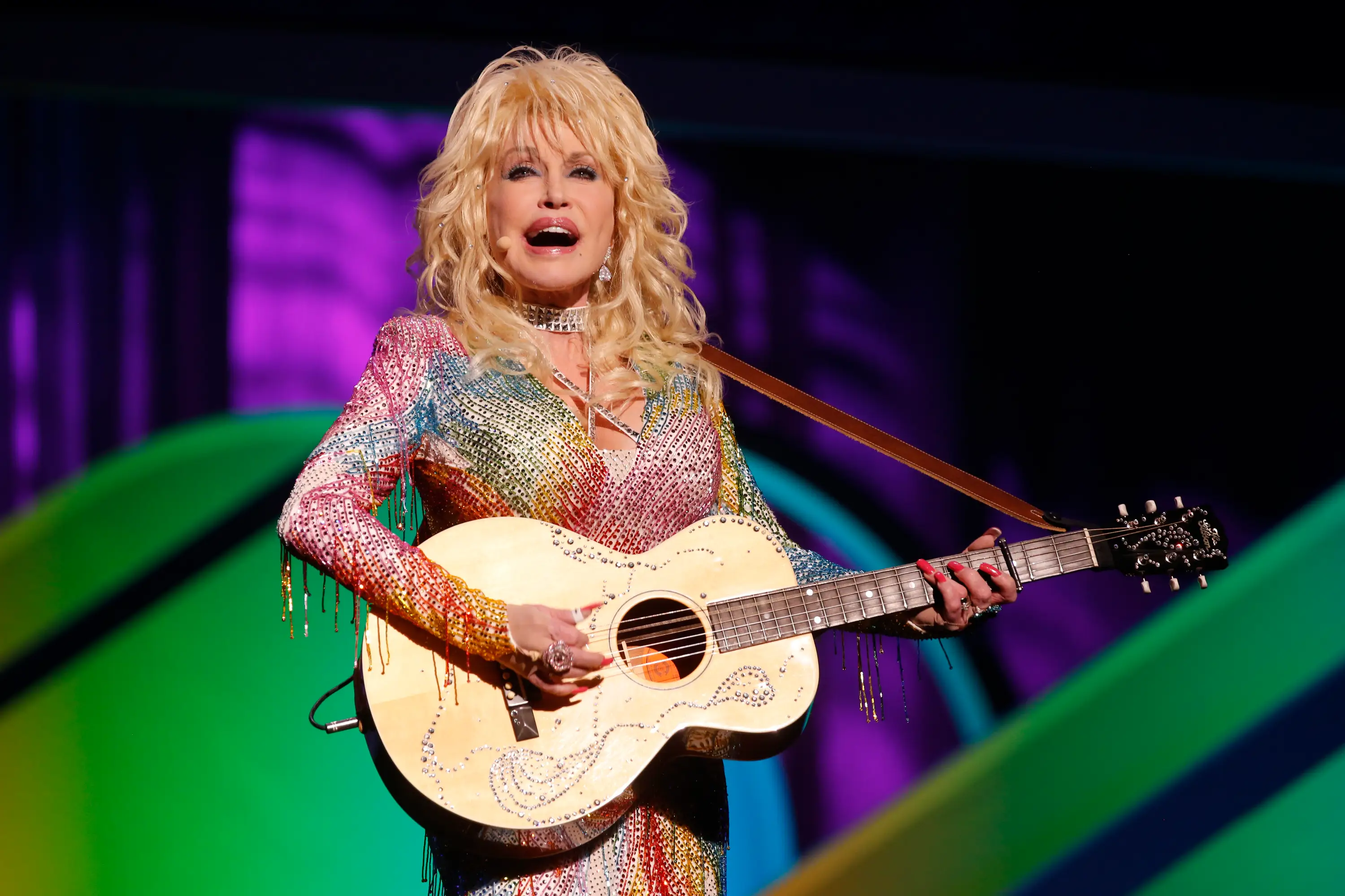 Dolly Parton with a guitar, singing, in a colorful, sparkly outfit