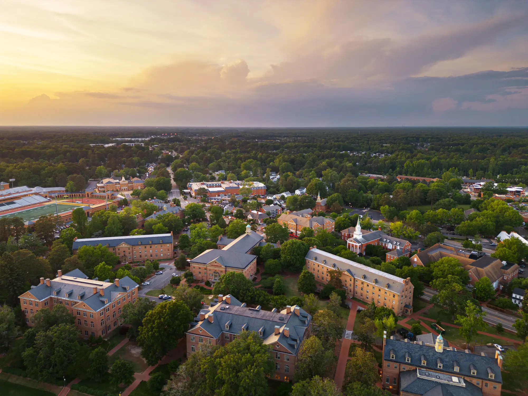 Aerial view of Williamsburg, Virginia, with academic buildings and an athletic field at sunset.