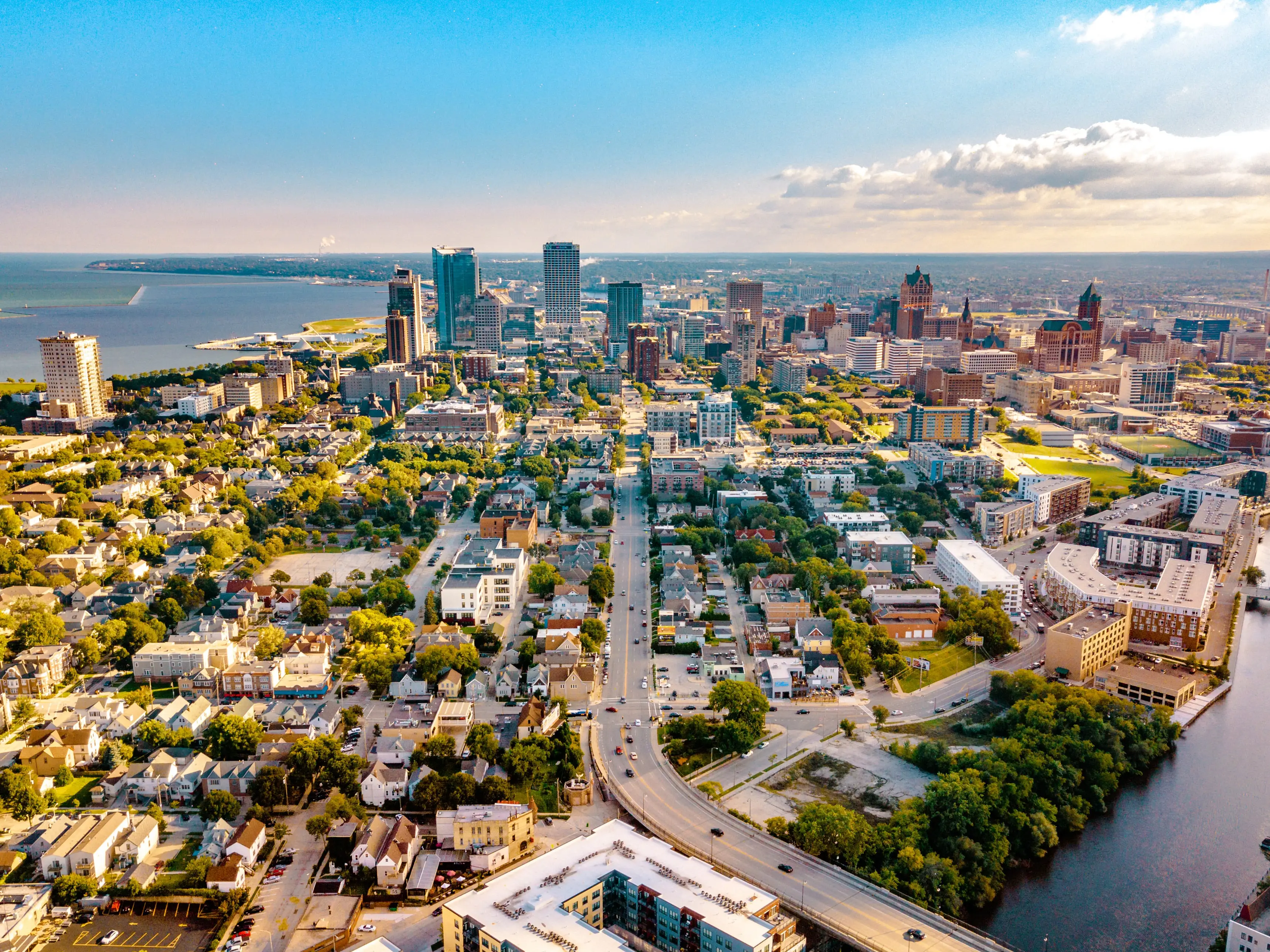 Aerial view of downtown Milwaukee skyline with surrounding neighborhoods, Lake Michigan, and the Milwaukee River at sunset.