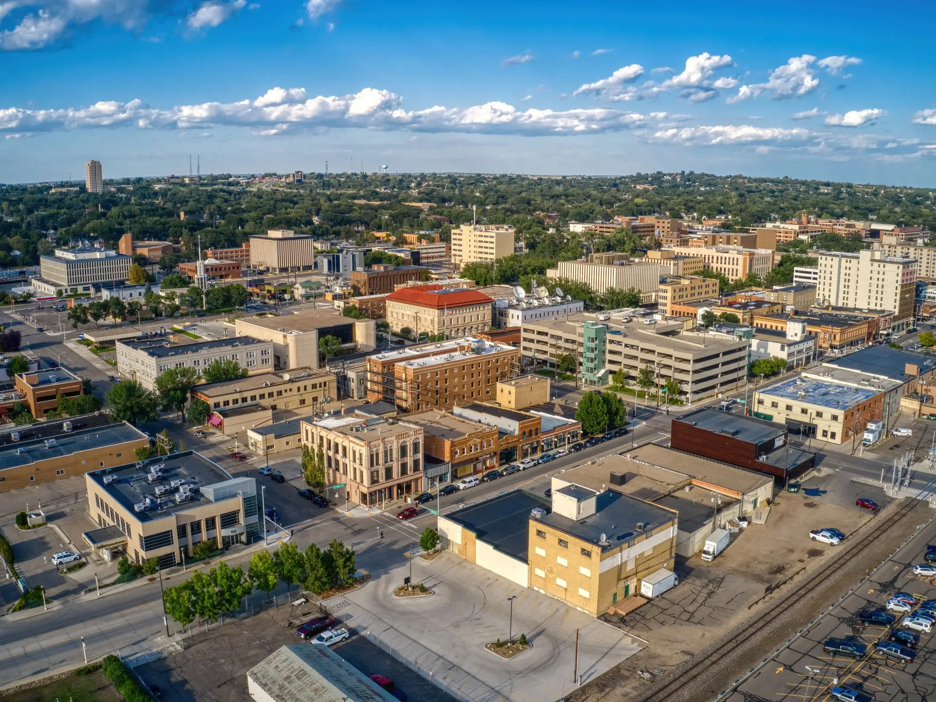 Aerial view of a downtown district with office buildings, streets, parking lots, and a partly cloudy sky.