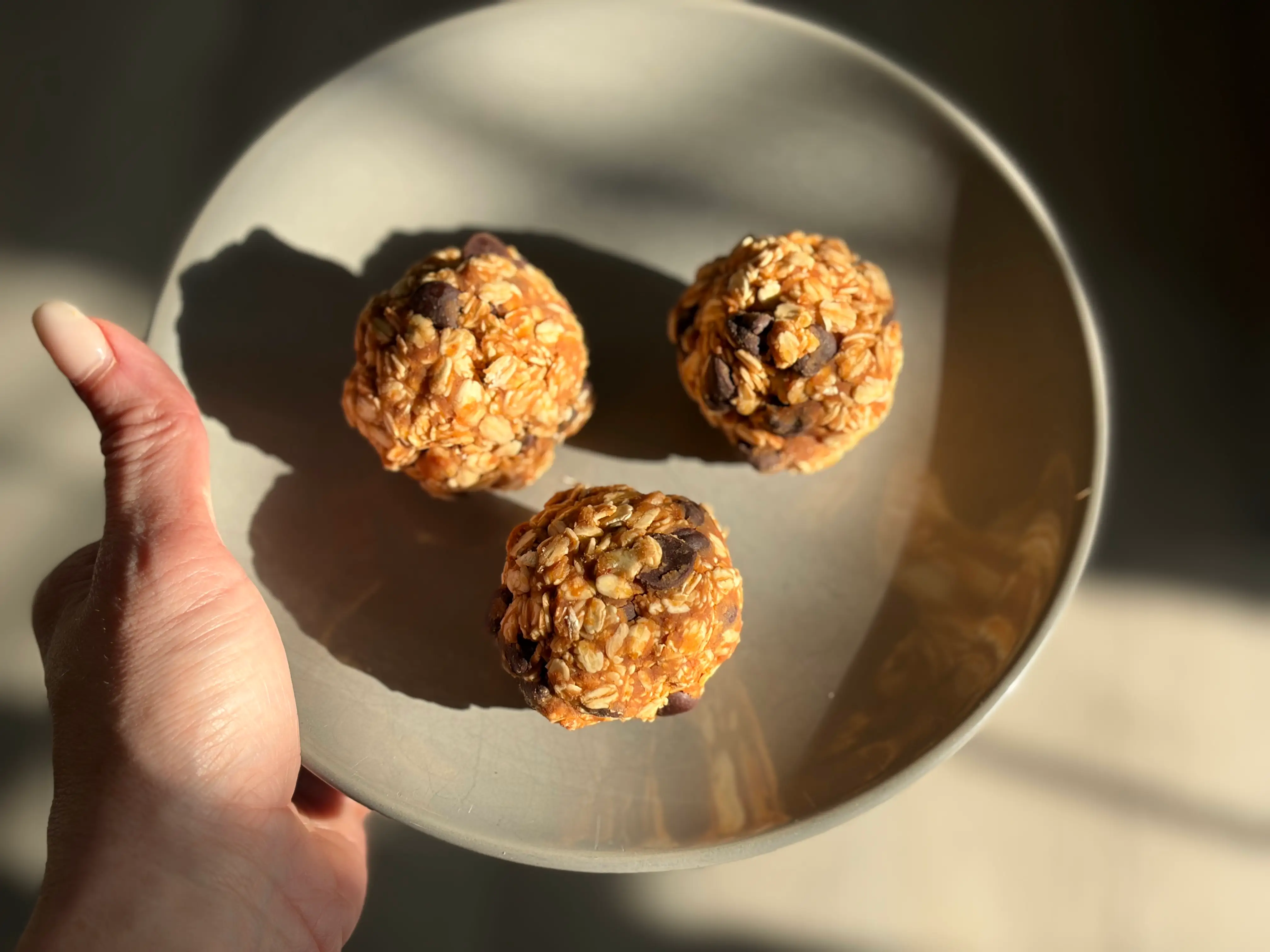 A hand holding a dish with three peanut-butter oat balls.