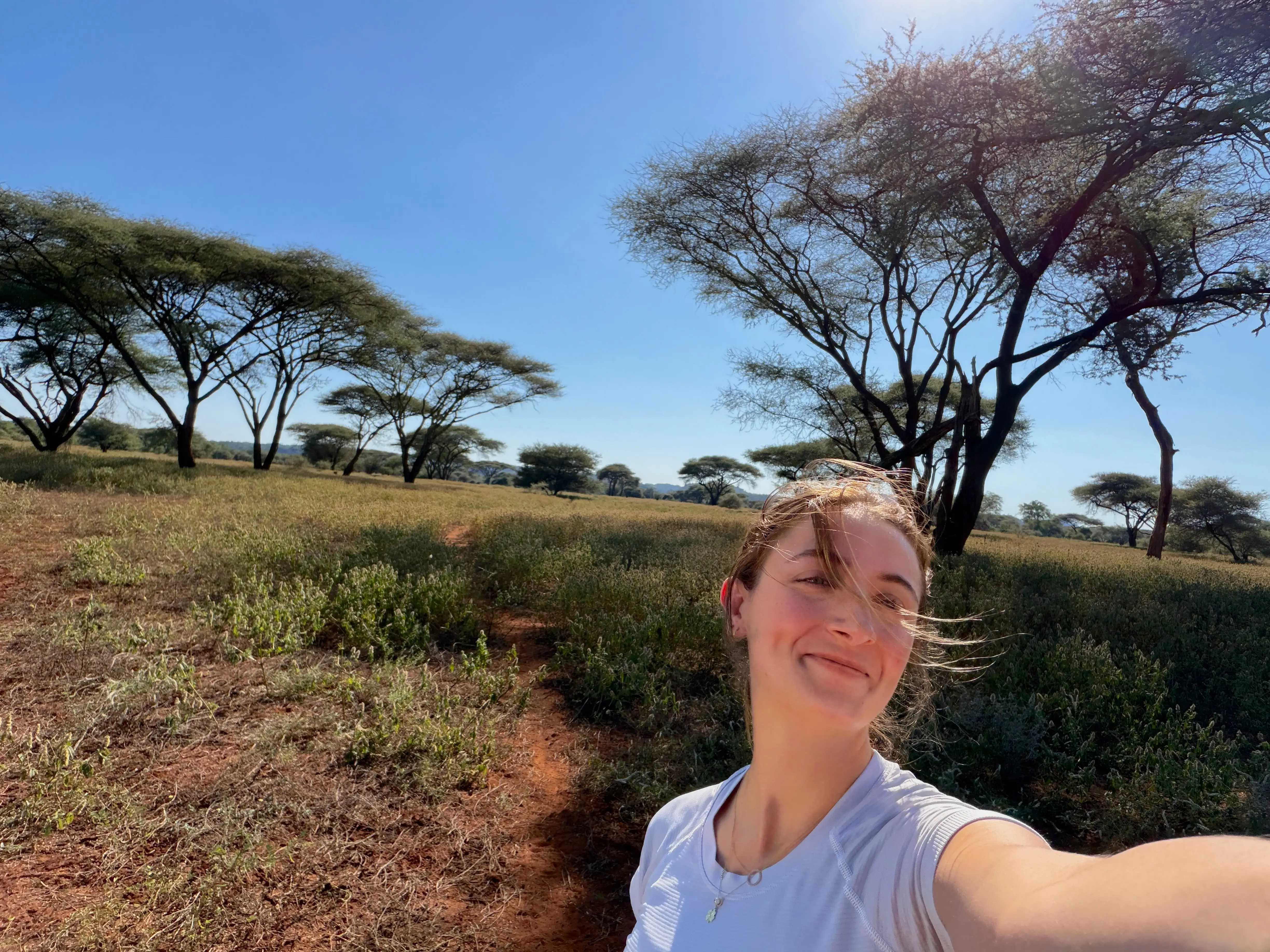The writer is posing for a selfie in a grassy field in Zimbabwe.