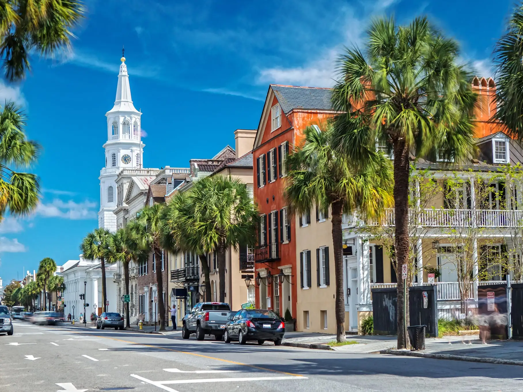Palm-lined historic street with colorful buildings and a white church steeple under a blue sky.