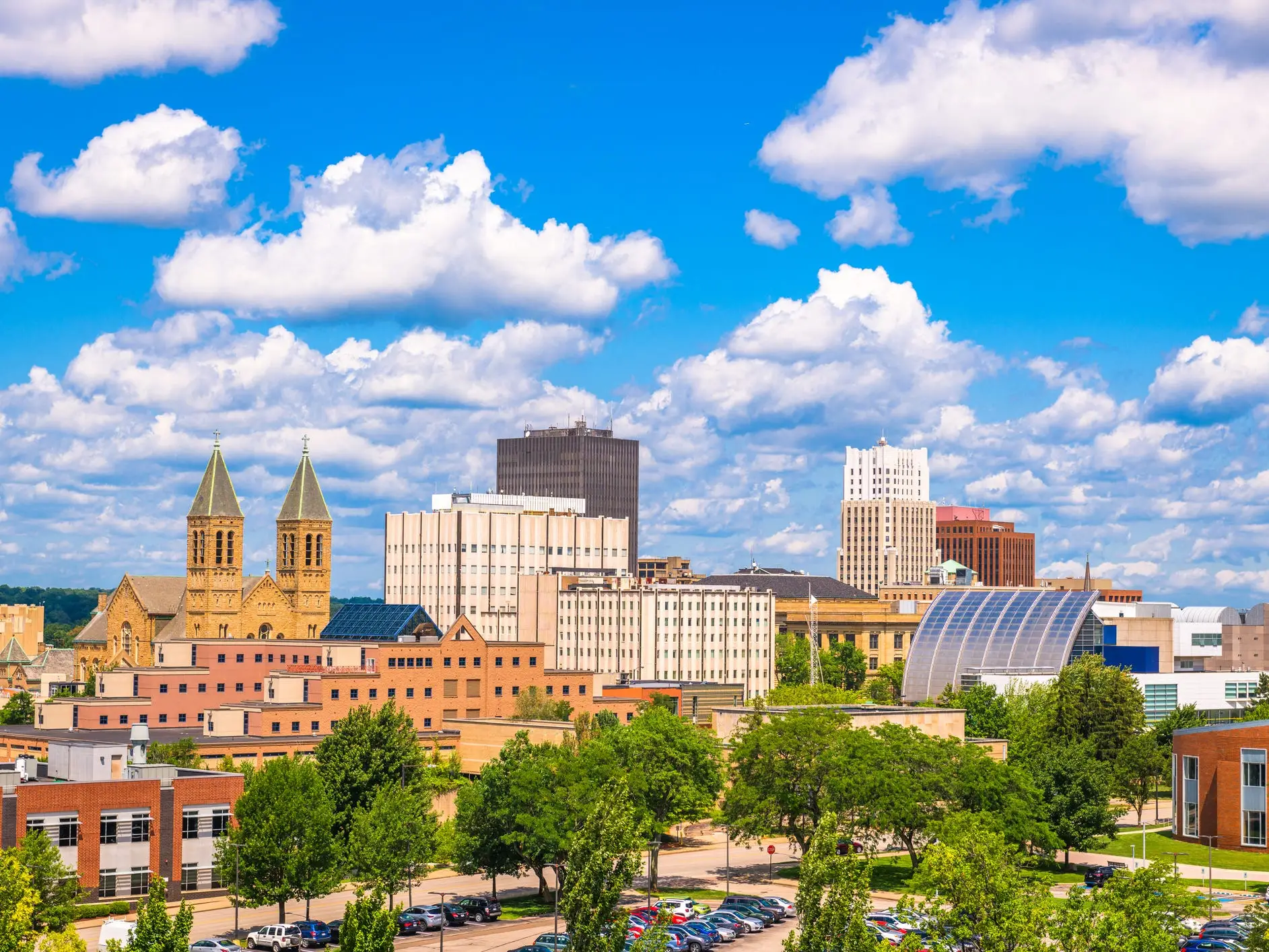 Downtown Akron skyline with church twin spires, office buildings, trees, and a blue sky filled with clouds.