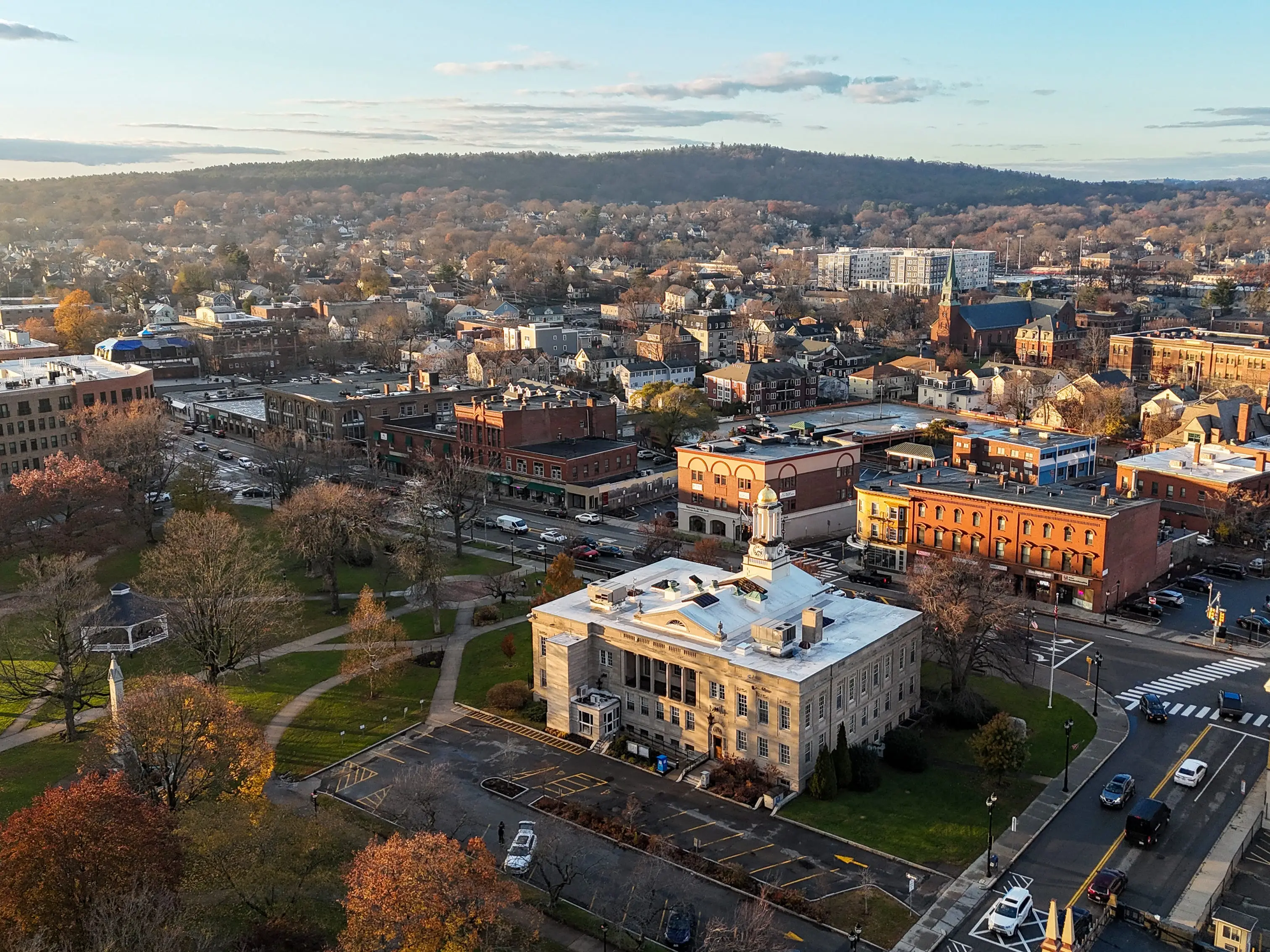 Aerial view of a downtown district with a domed civic building, park, streets, and autumn trees.