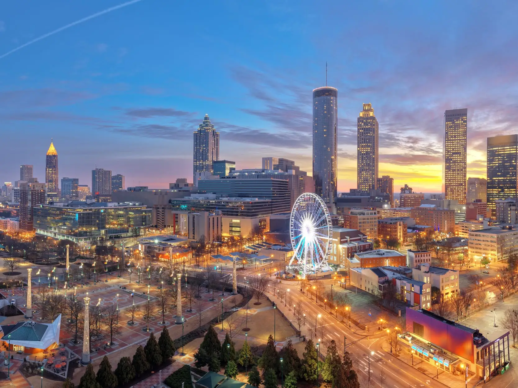 Downtown Atlanta skyline at sunset with illuminated high-rises, streets, parks, and the SkyView Atlanta Ferris wheel.