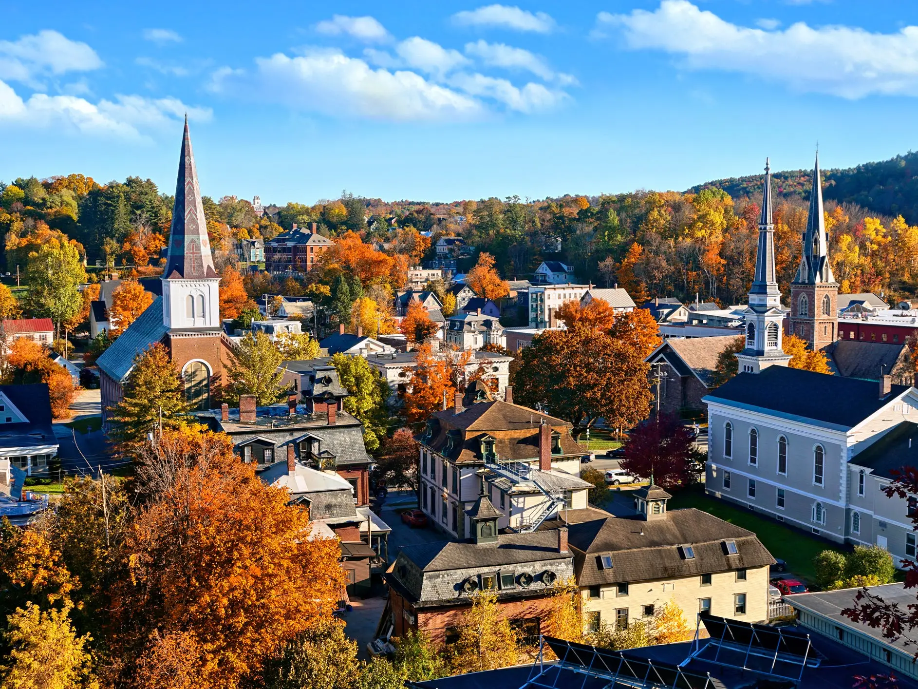 Autumn foliage surrounds a small town with multiple church steeples under a bright blue sky.