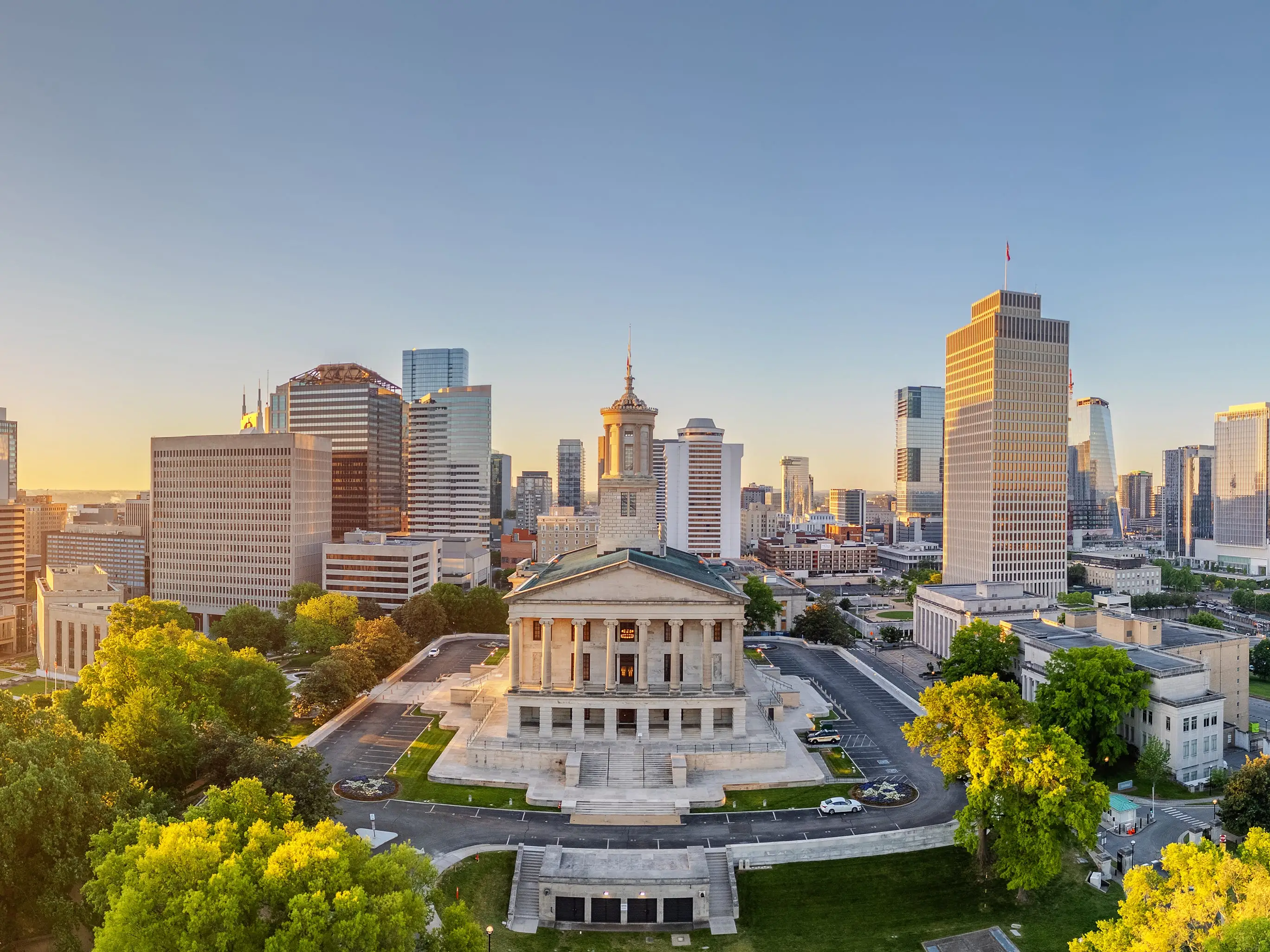 Tennessee State Capitol stands amid downtown Nashville skyscrapers at golden hour.