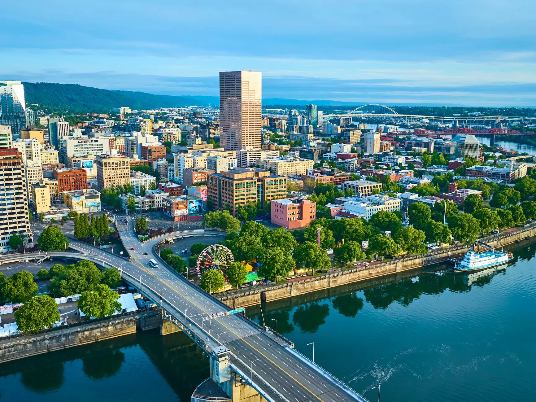 Downtown Portland skyline rises beside the Willamette River with bridges, waterfront trees, and a ferris wheel.