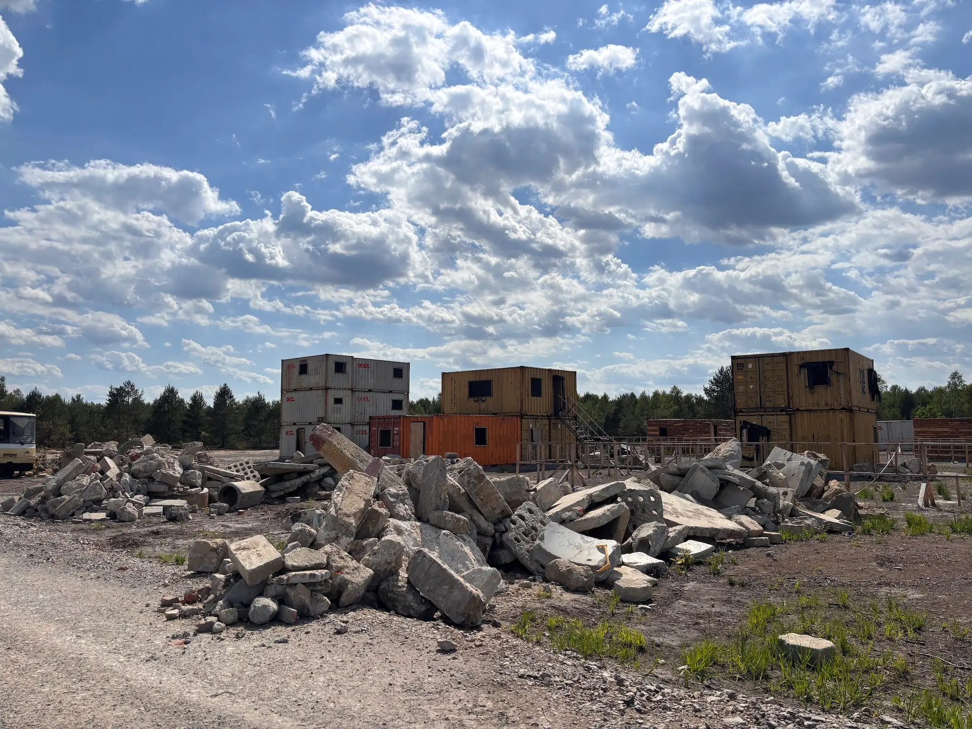 Concrete rubble piles sit in front of stacked shipping containers at an outdoor work site under a cloudy sky.