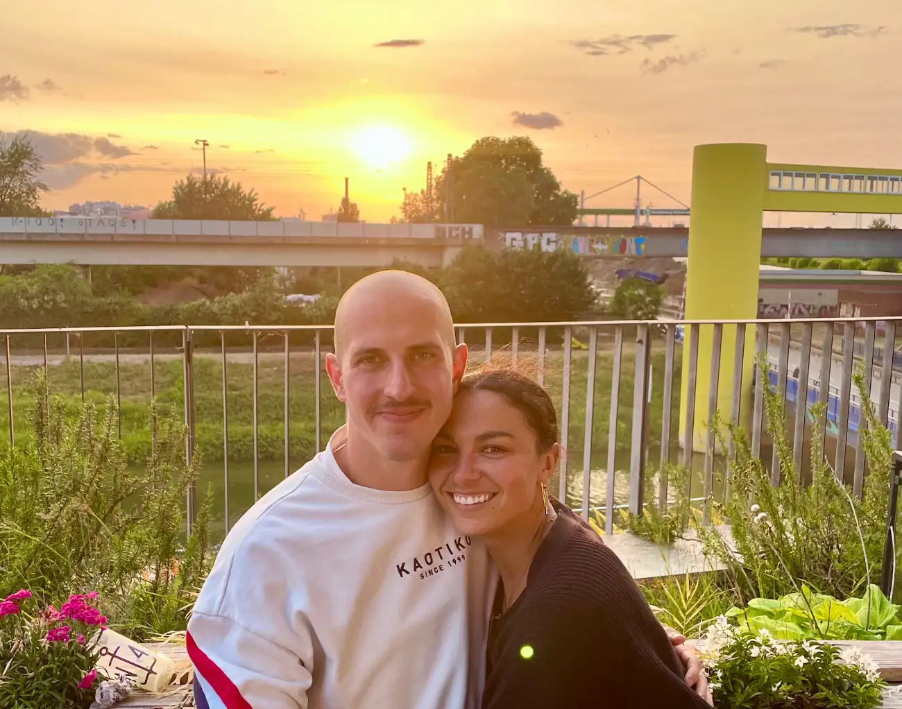 The writer and her partner hold each other in a garden while the sun sets in the background.