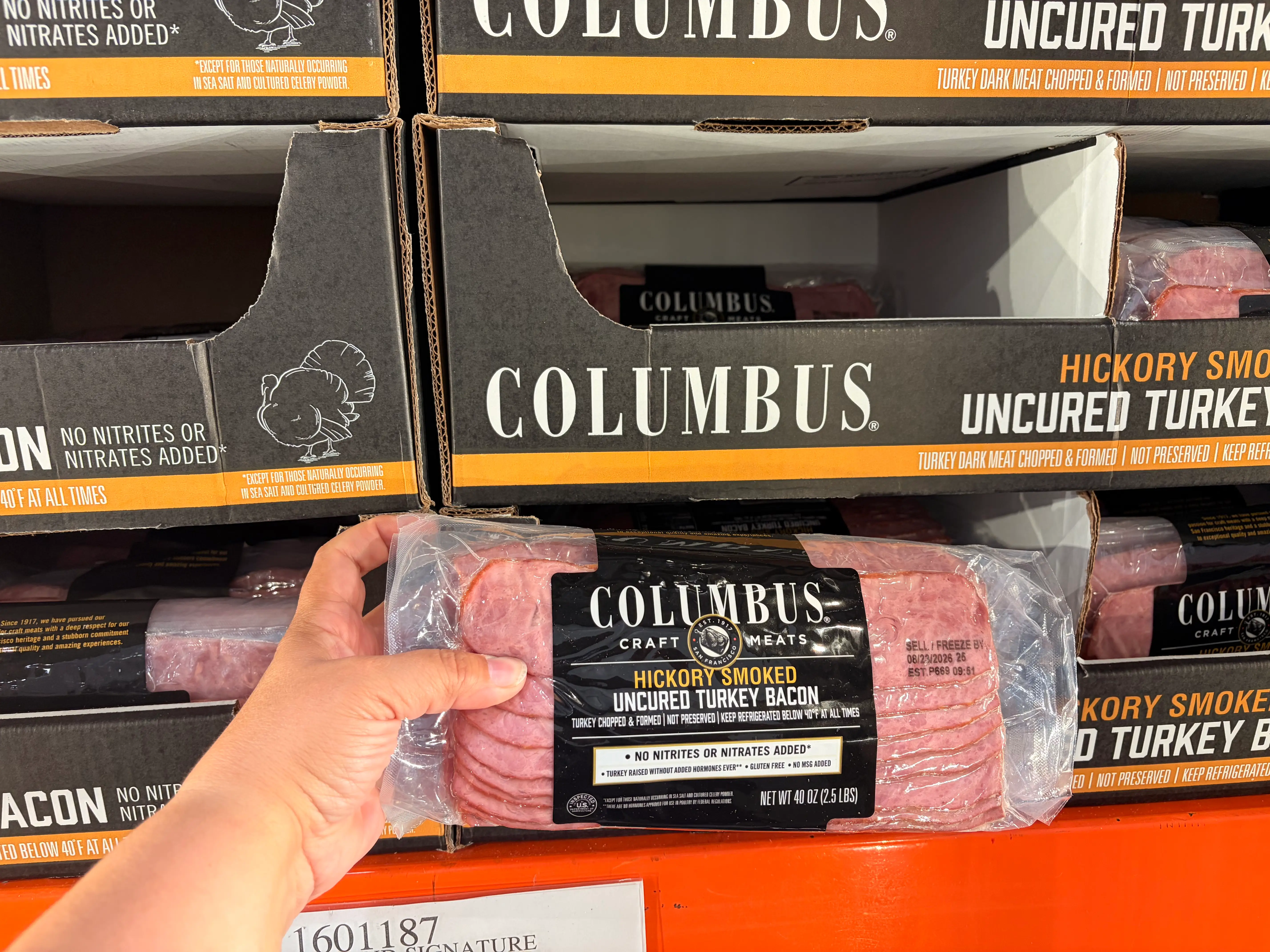 A hand holding a package of Columbus turkey bacon.