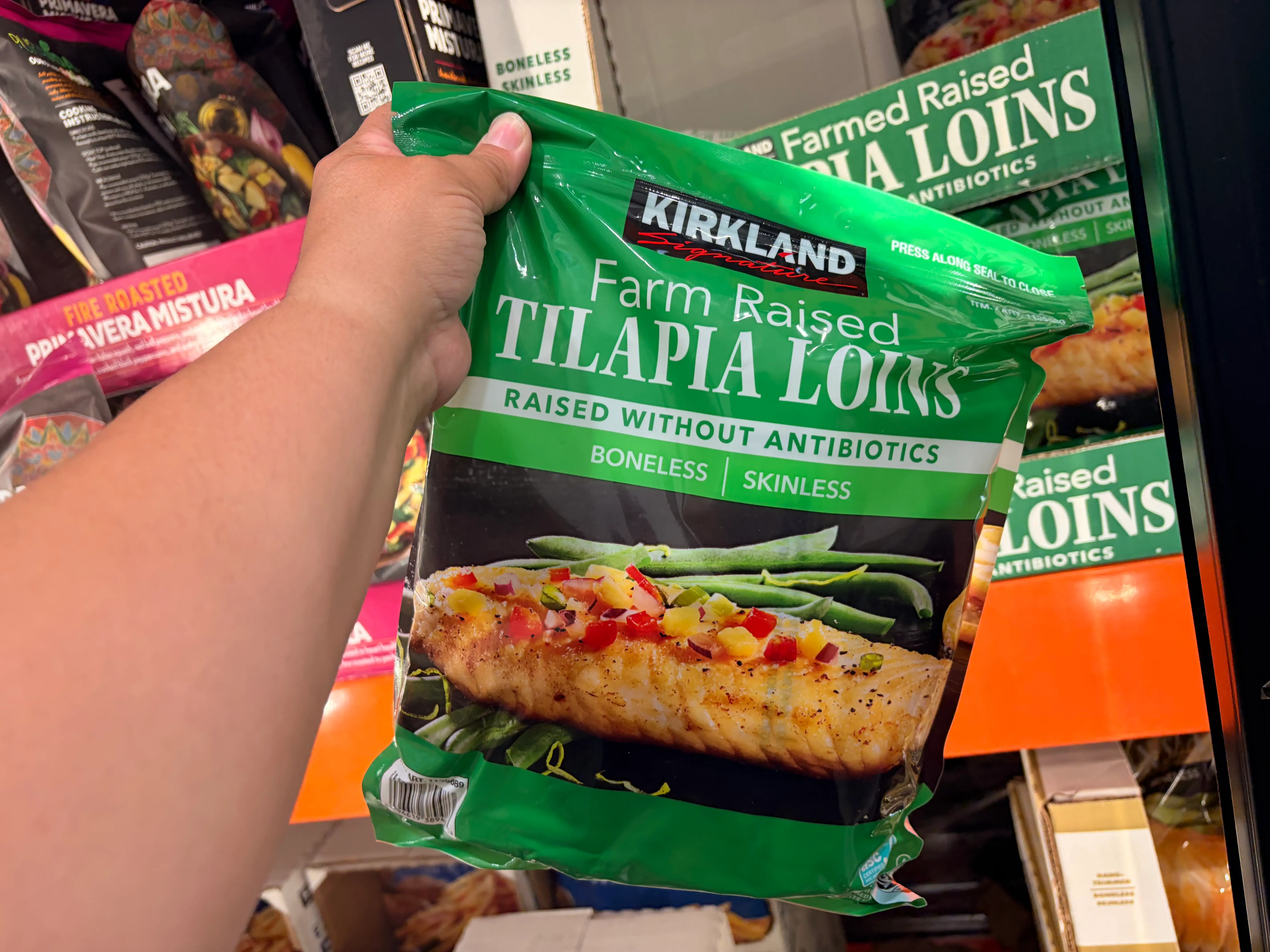A hand holding a bag of Kirkland Signature farm-raised tilapia loins.
