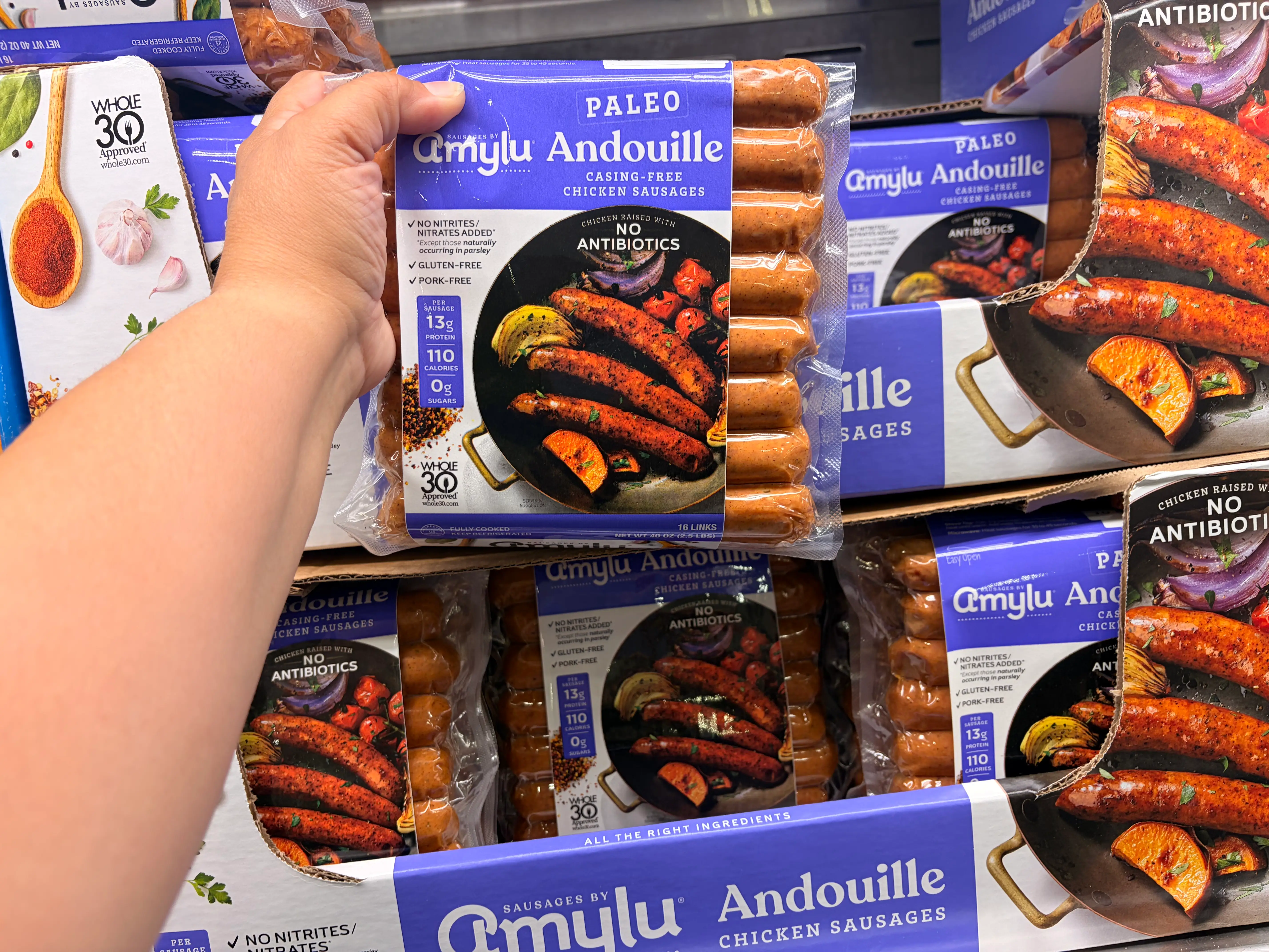 A hand holding a package of Amylu andouille chicken sausage.