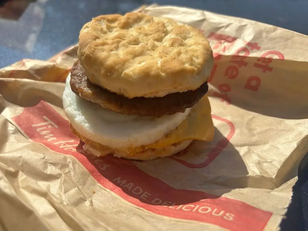 A sausage, egg, and cheese sandwich on an English muffin, sitting on a bag from Tim Hortons.