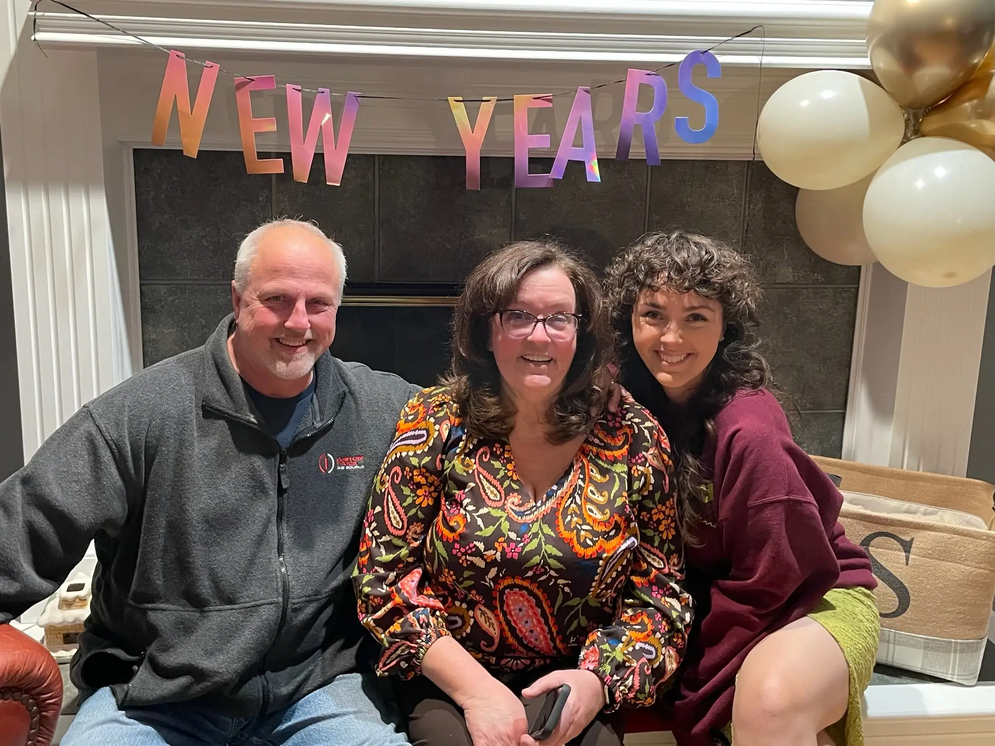 Woman and her parents smiling in front of New Years baner on fireplace