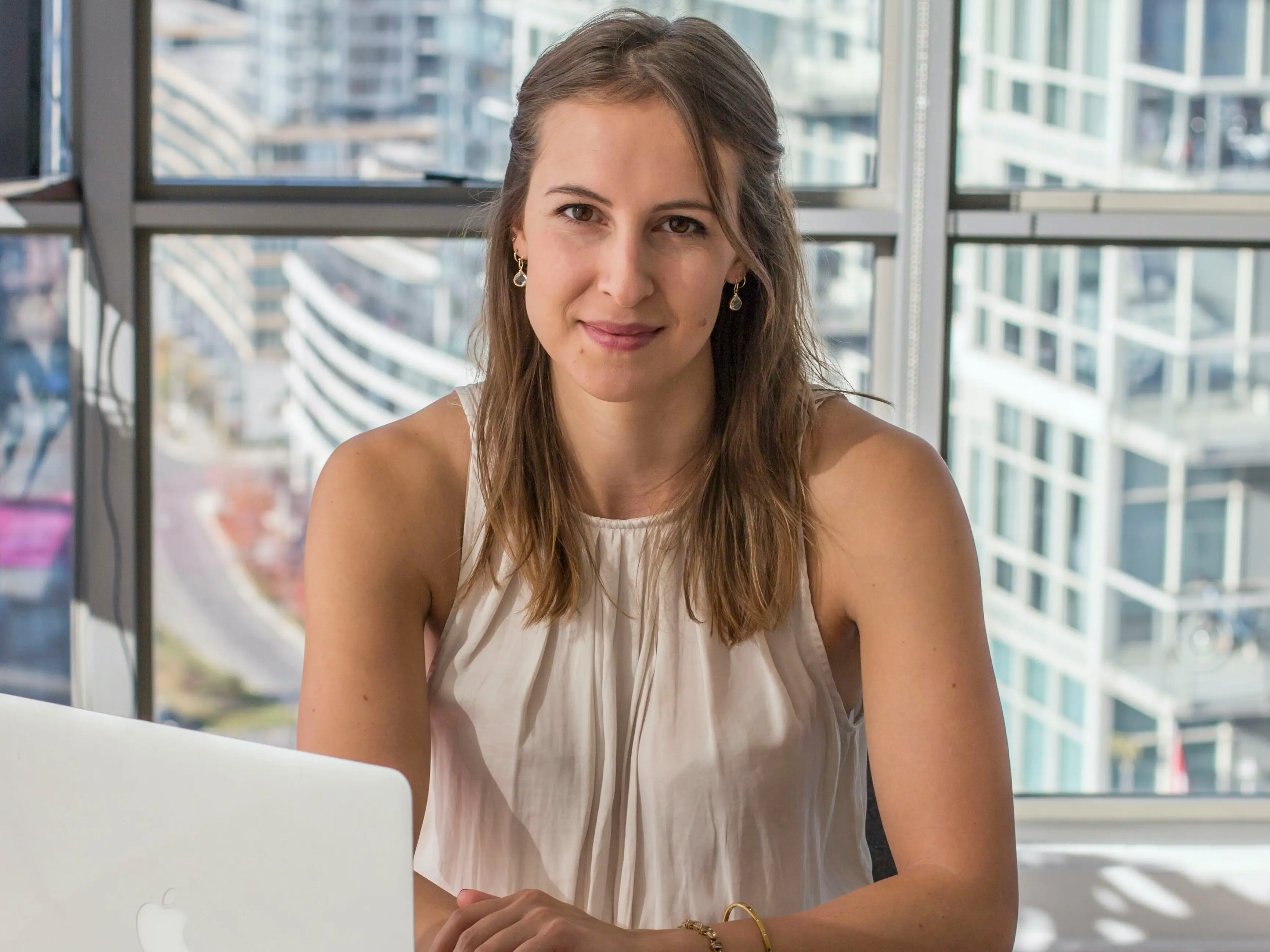 Valerie Crisp, headshot, sitting at a desk holding a pen with a laptop and an open notebook in front of her on the desk.