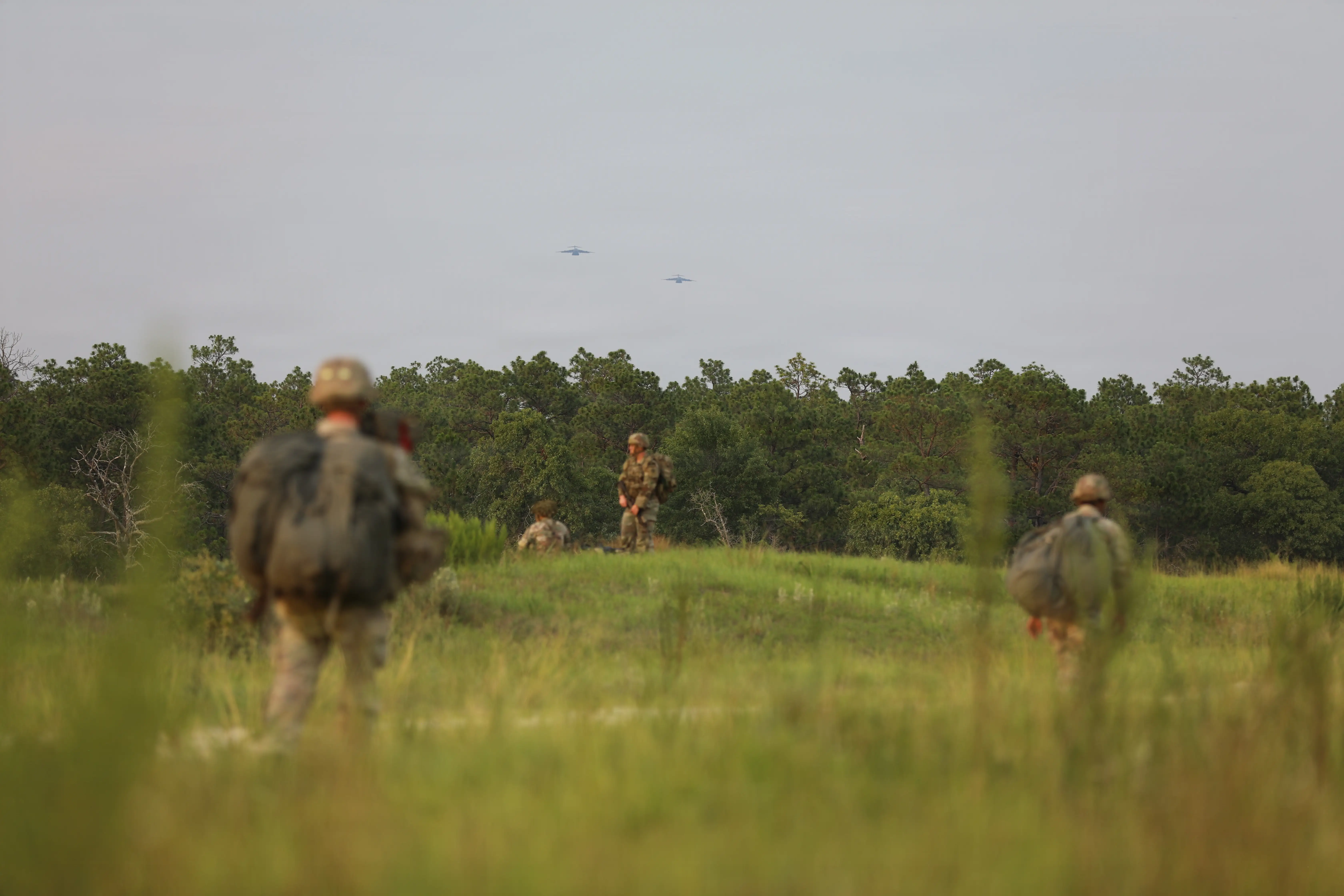 Soldiers are seen gathered in a grassy field surrounded by trees.