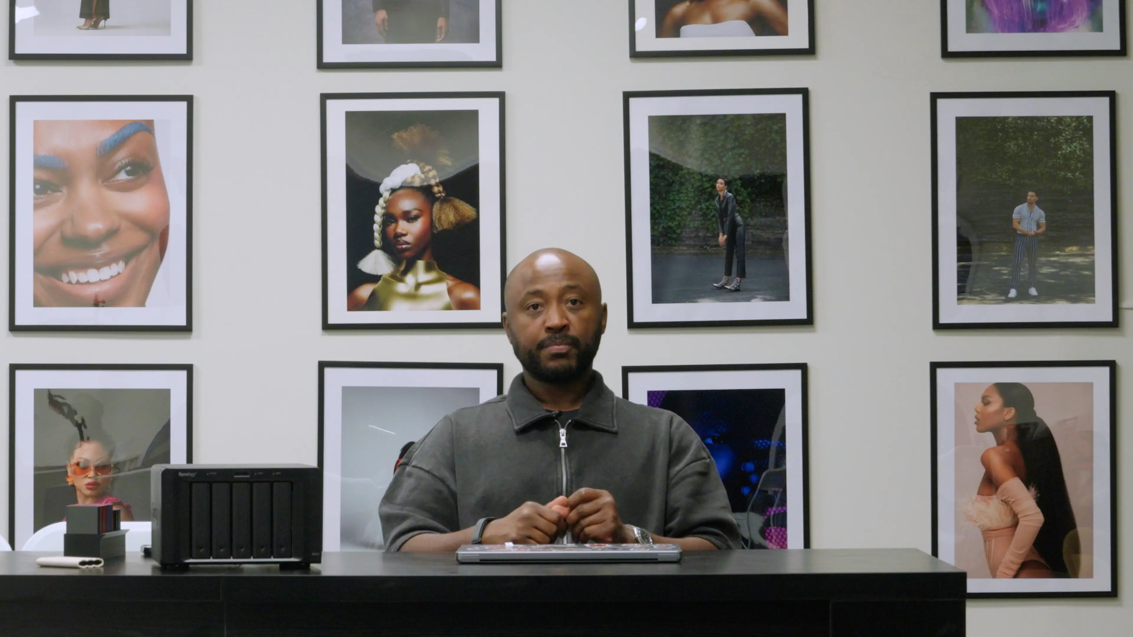 Allen Cooley sits at a desk in front of framed photos he's taken over his career as a professional commercial photographer.