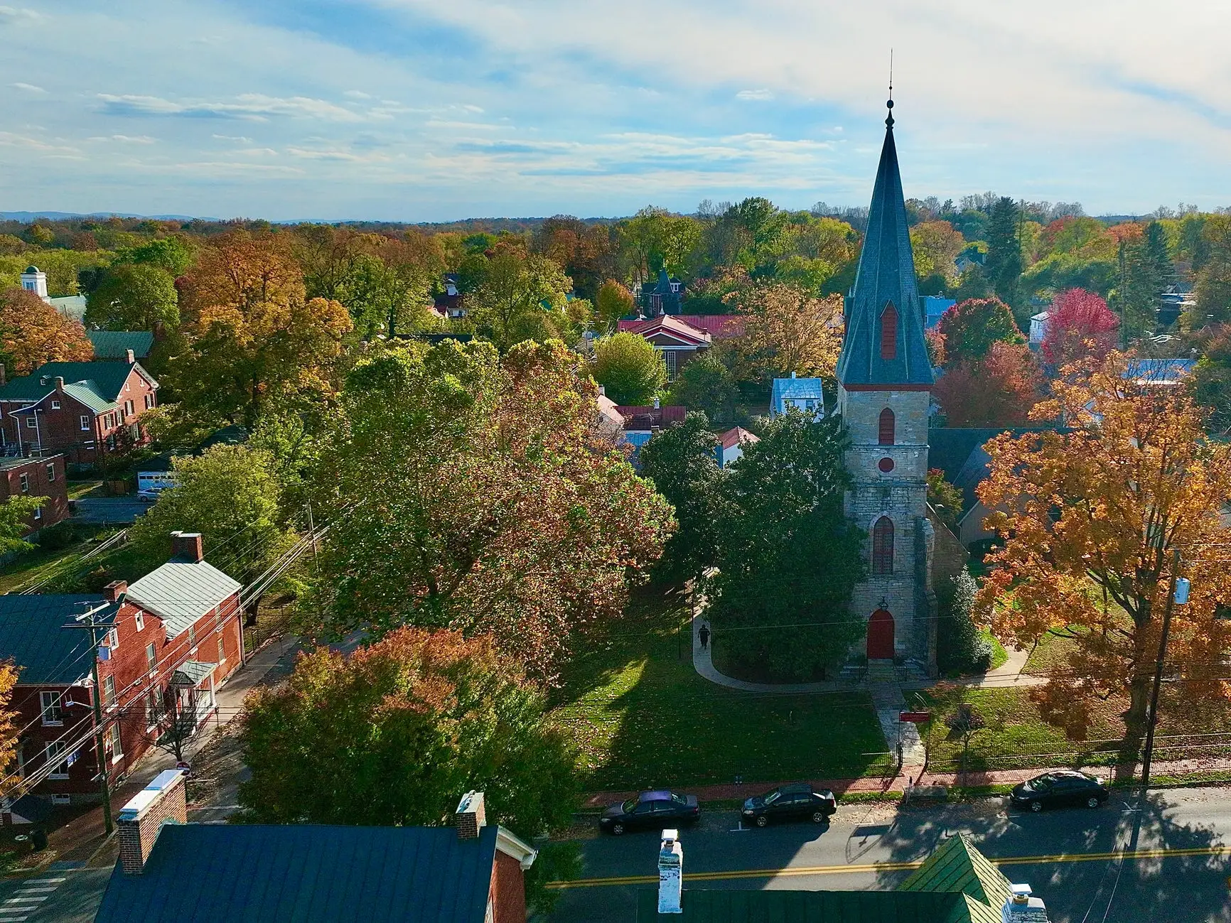 Aerial view of  Shepherdstown with a small town church steeple surrounded by autumn trees, houses, streets, and parked cars.