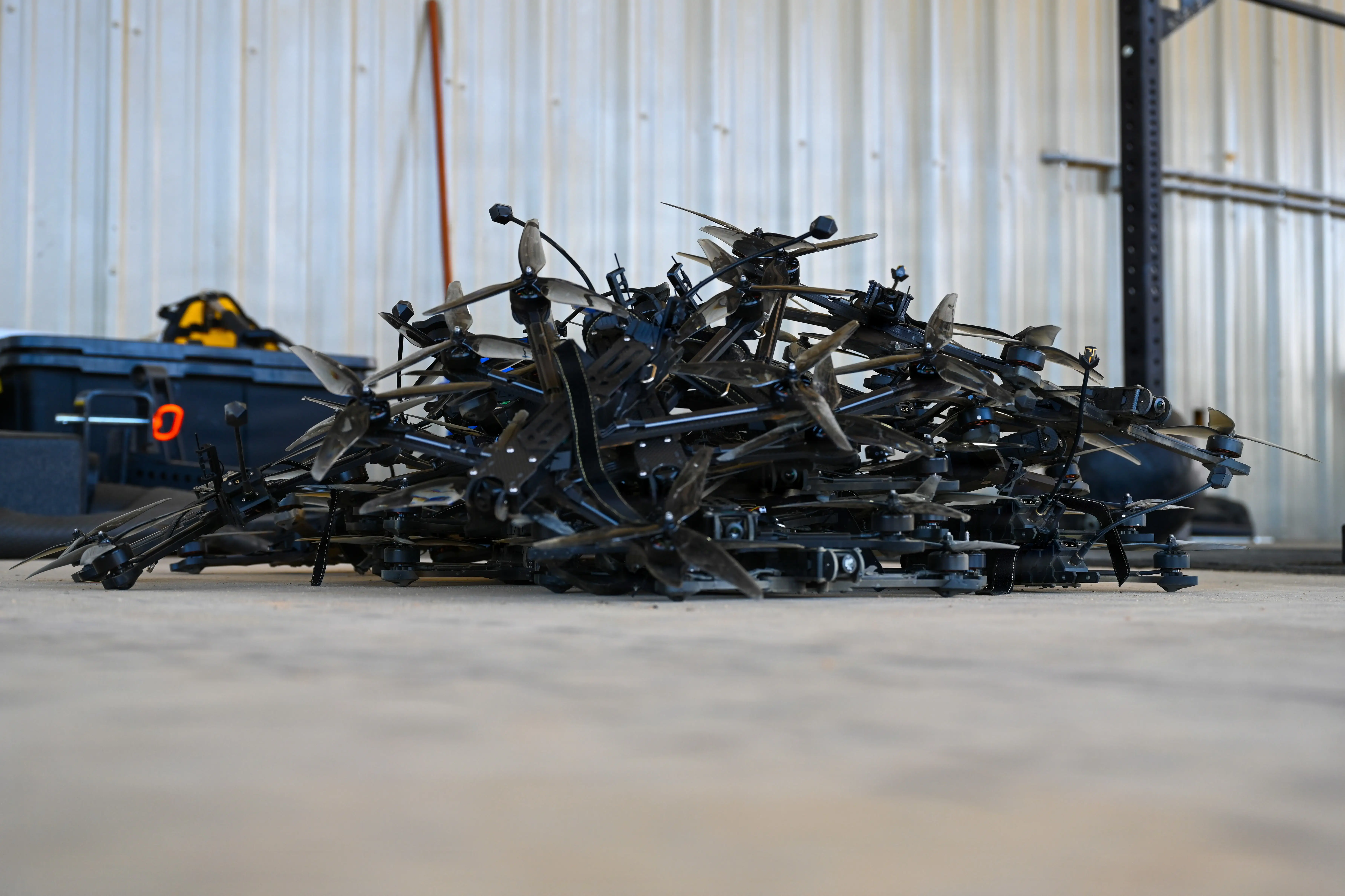 A pile of destroyed small black drones sits in a warehouse.