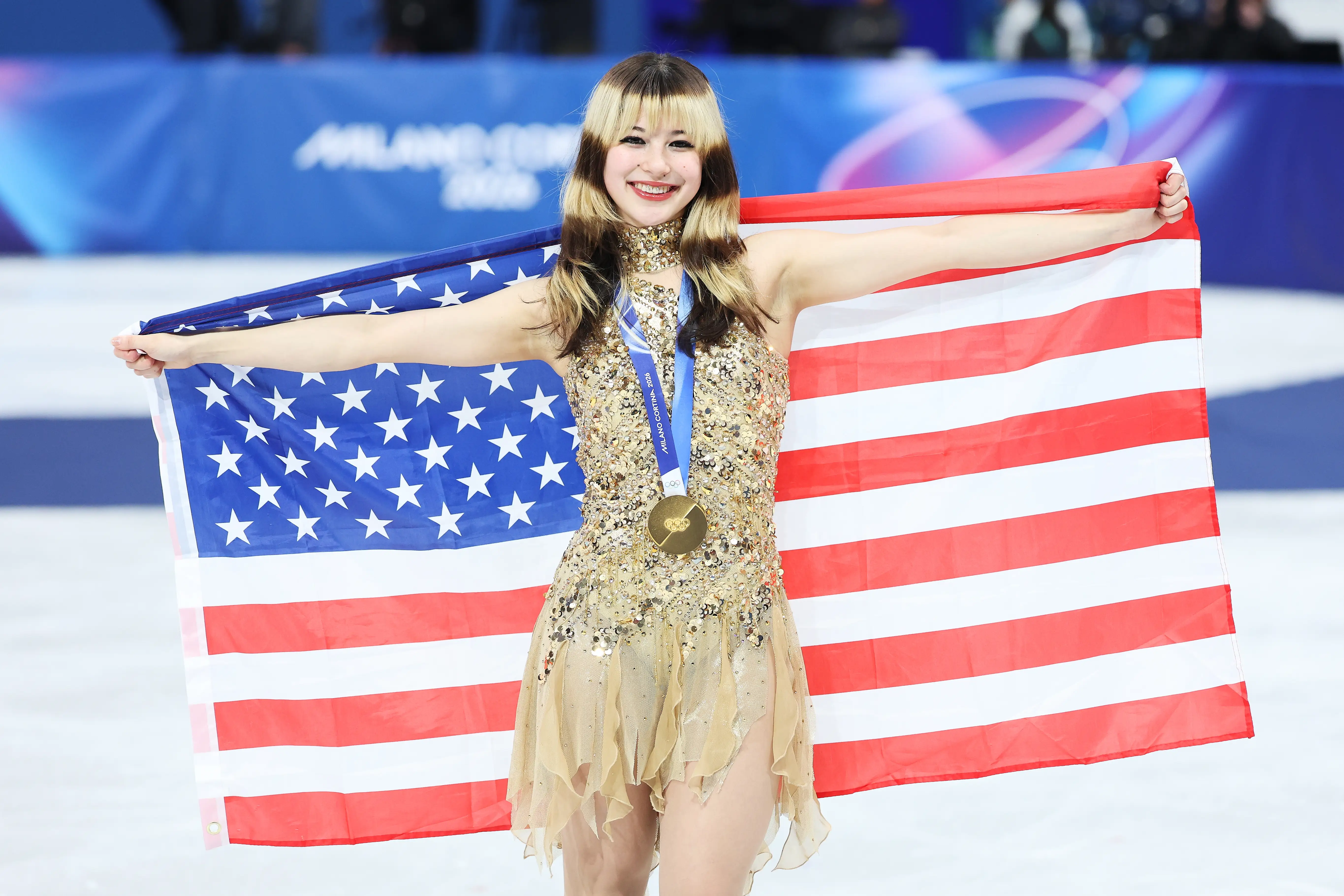 Figure skater holds a United States flag while wearing a medal on an ice rink.