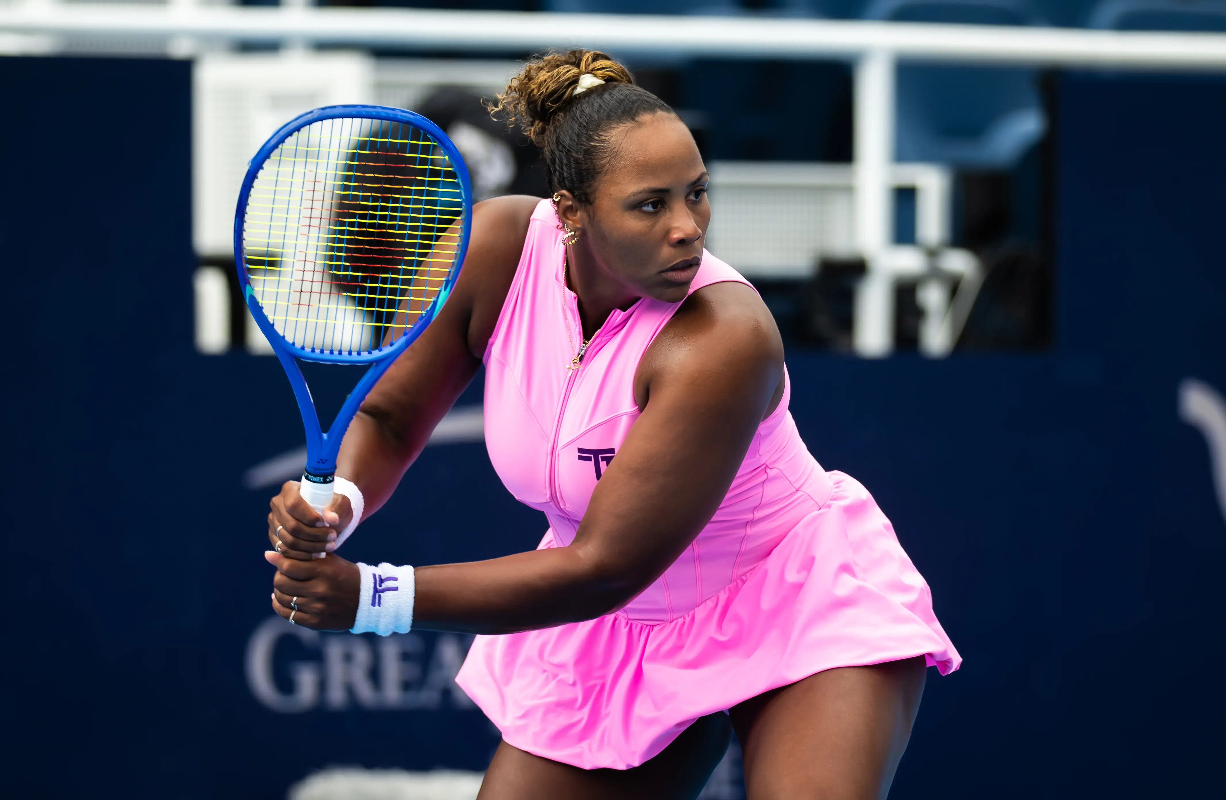 Taylor Townsend prepares a backhand with a blue racket while wearing a pink tennis dress on court.