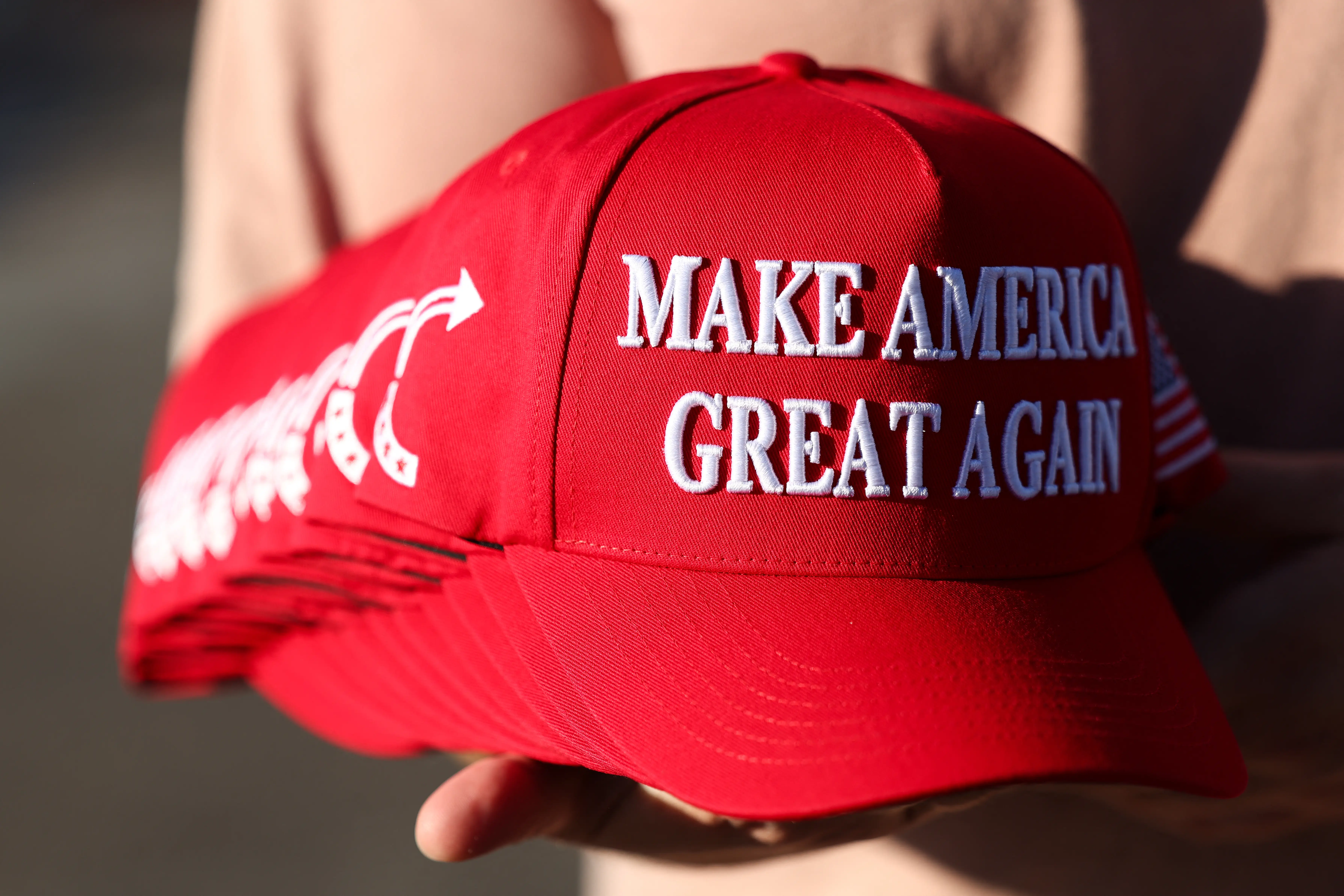 A member of Turning Point USA distributes MAGA hats to people gathered at a makeshift memorial for right-wing activist and Turning Point USA founder Charlie Kirk outside of their headquarters in Phoenix, Arizona, on September 19, 2025.