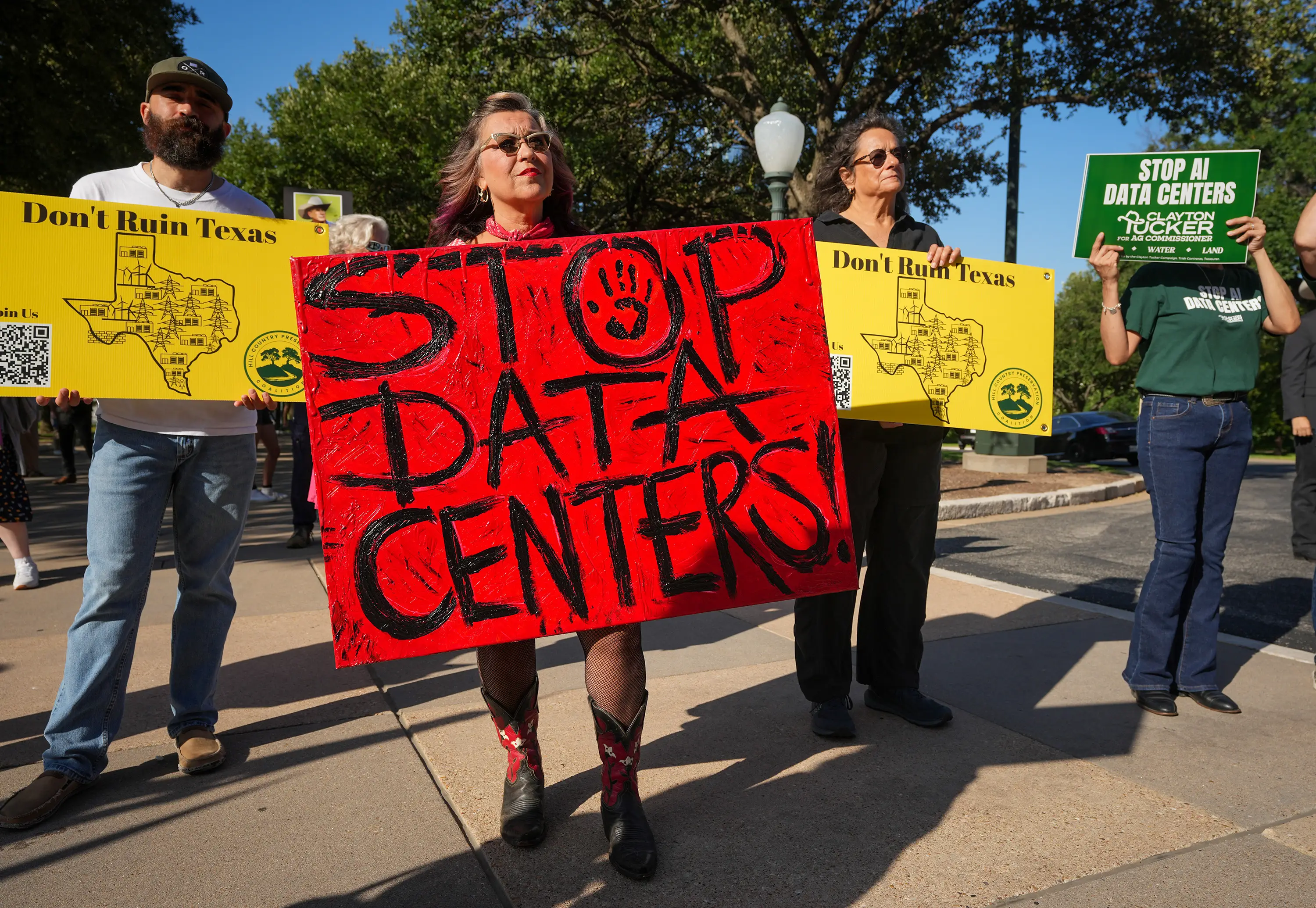 Protesters hold signs reading “STOP DATA CENTERS!” and “Don’t Ruin Texas” at an outdoor demonstration.