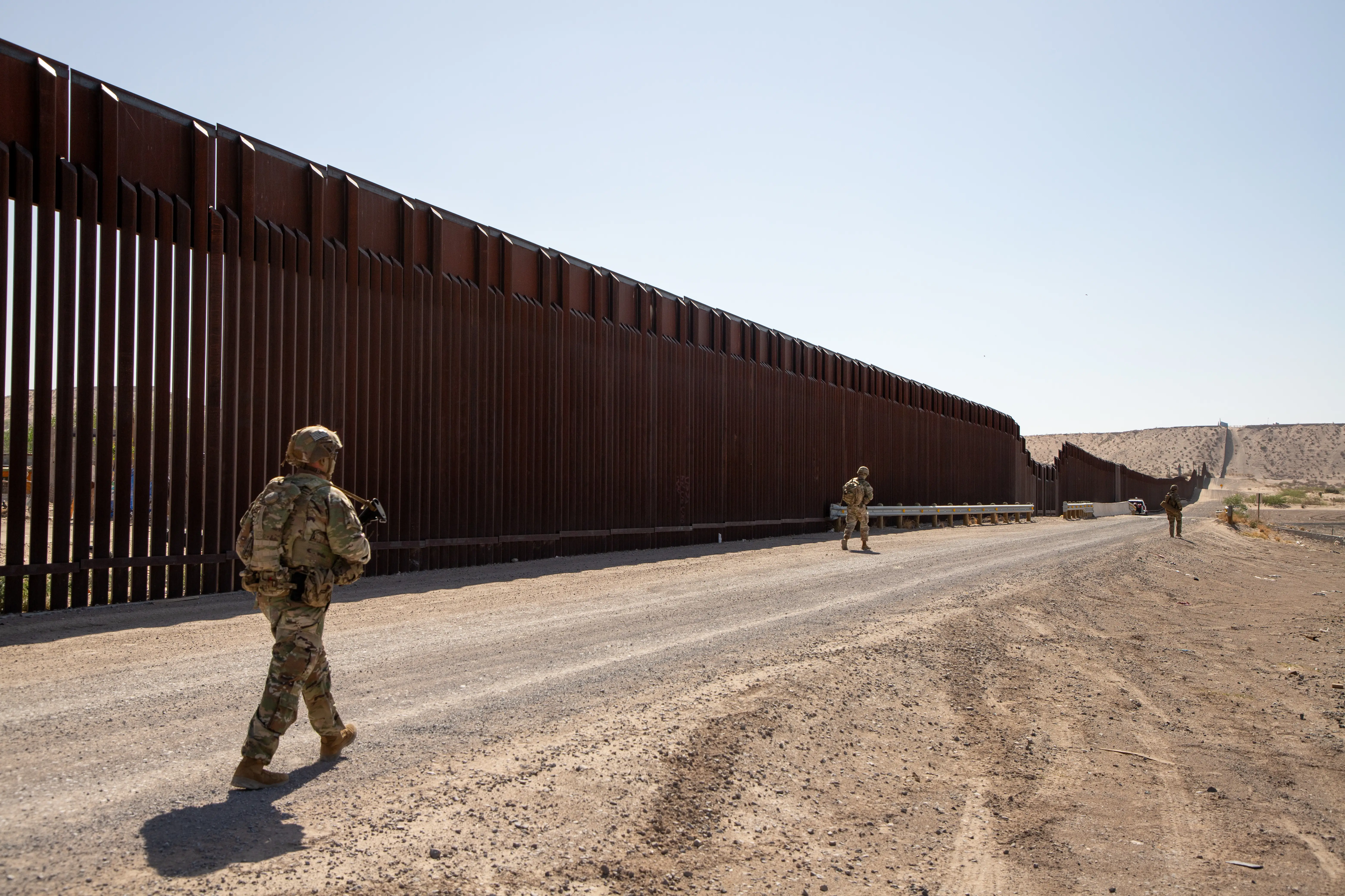 US soldiers walk along the southern border wall.