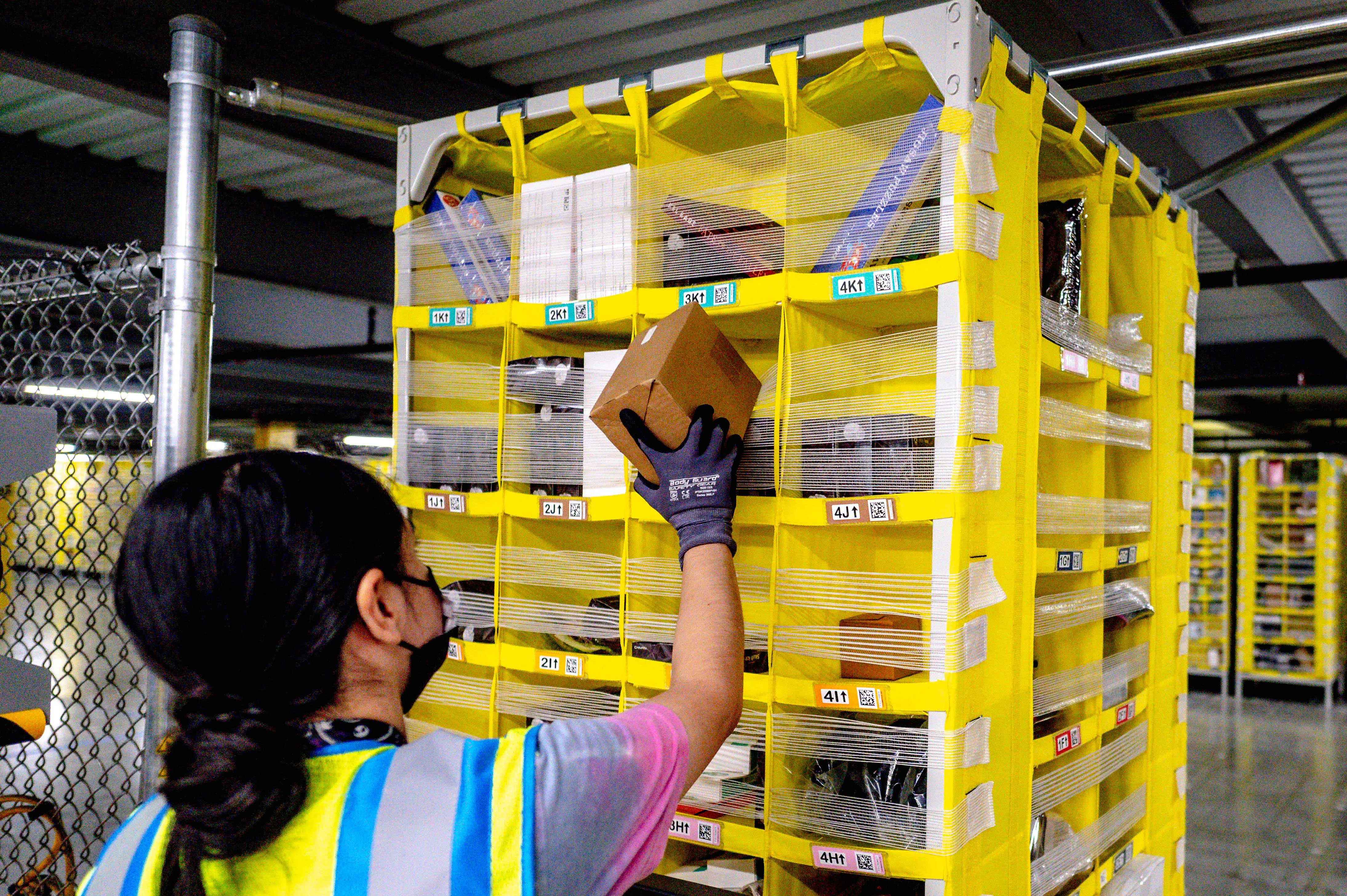 Warehouse worker places a cardboard parcel into a yellow sorting rack filled with mail and packages.
