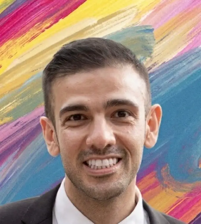 Smiling person in a dark jacket and white shirt poses before a colorful brushstroke mural.