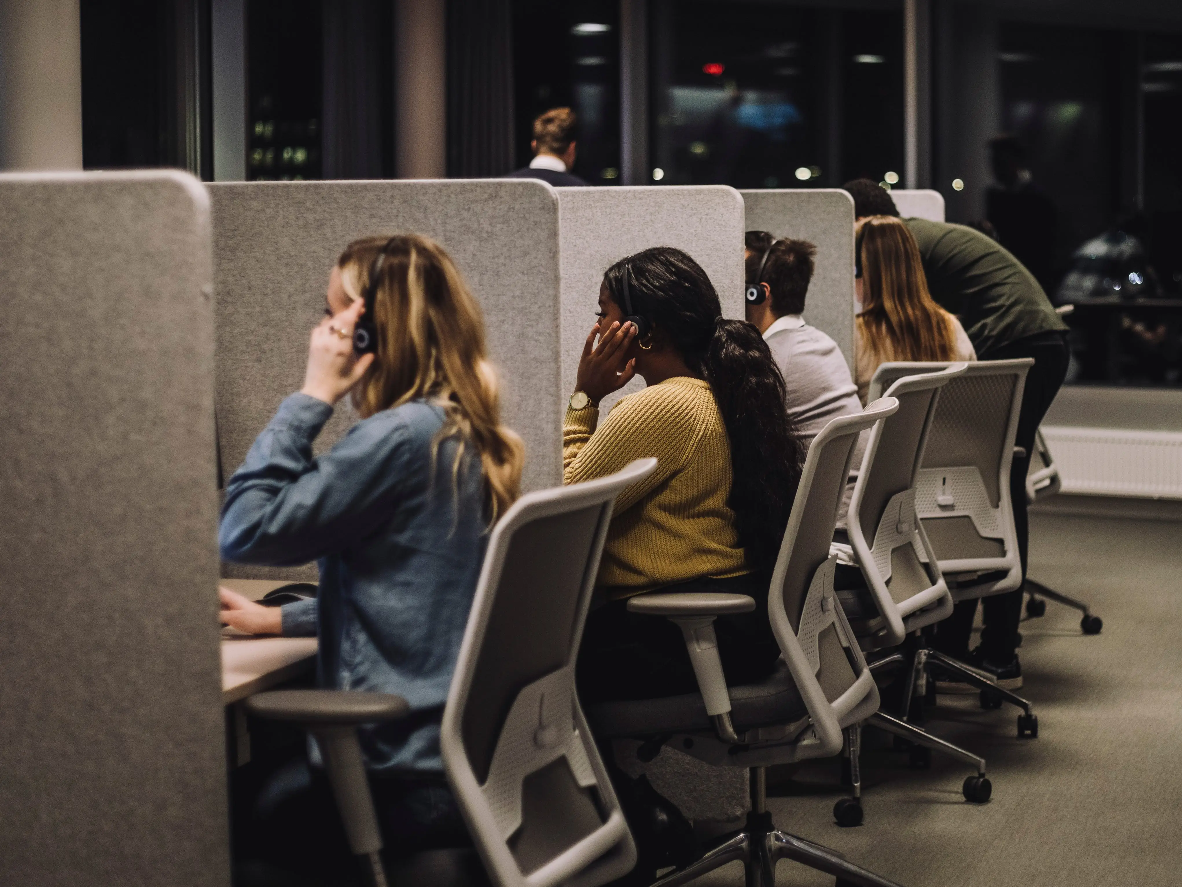 Workers wearing headsets sit at partitioned desks in an office