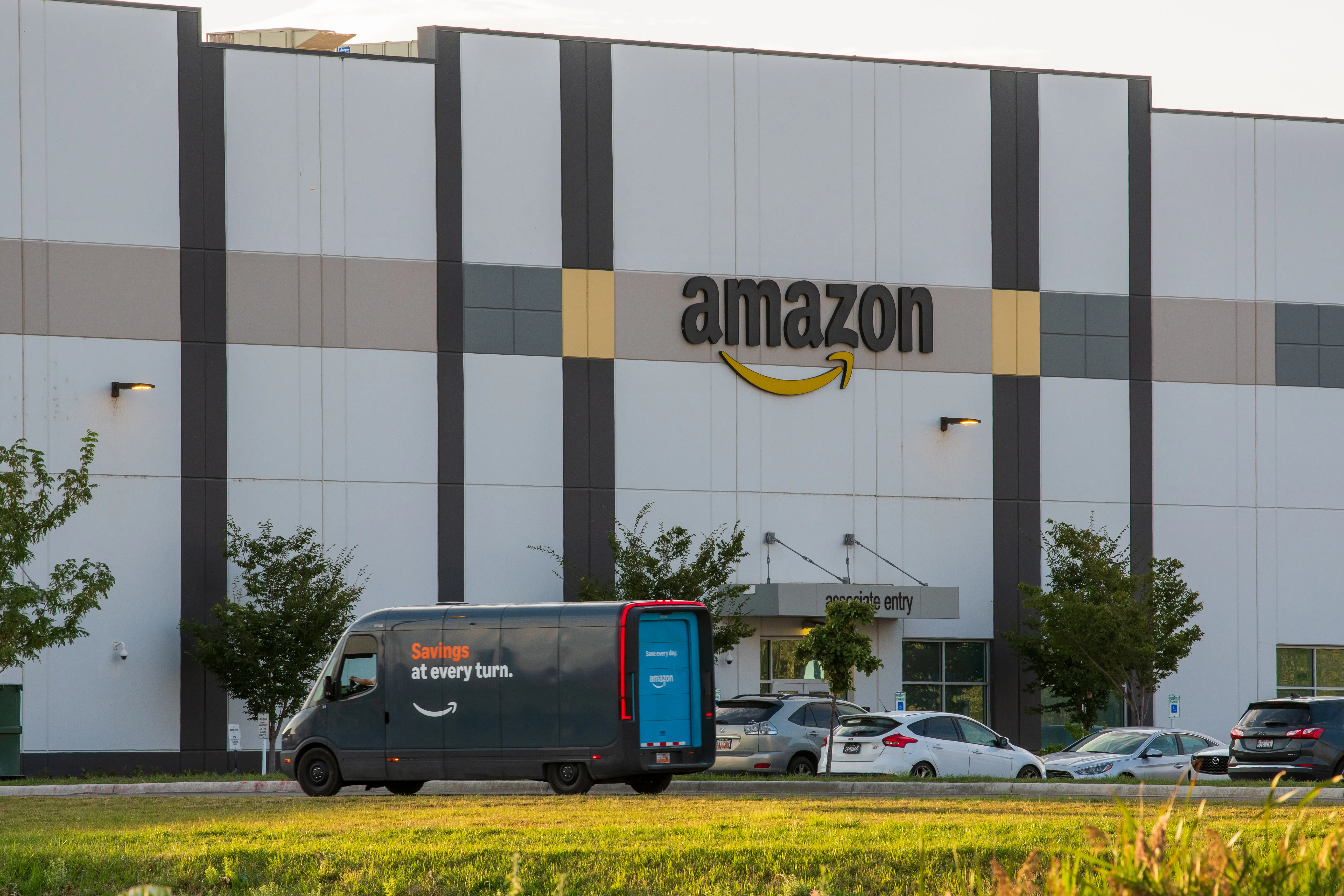 A delivery van outside of a large Amazon logistics facility with an Amazon logo on it in Utah