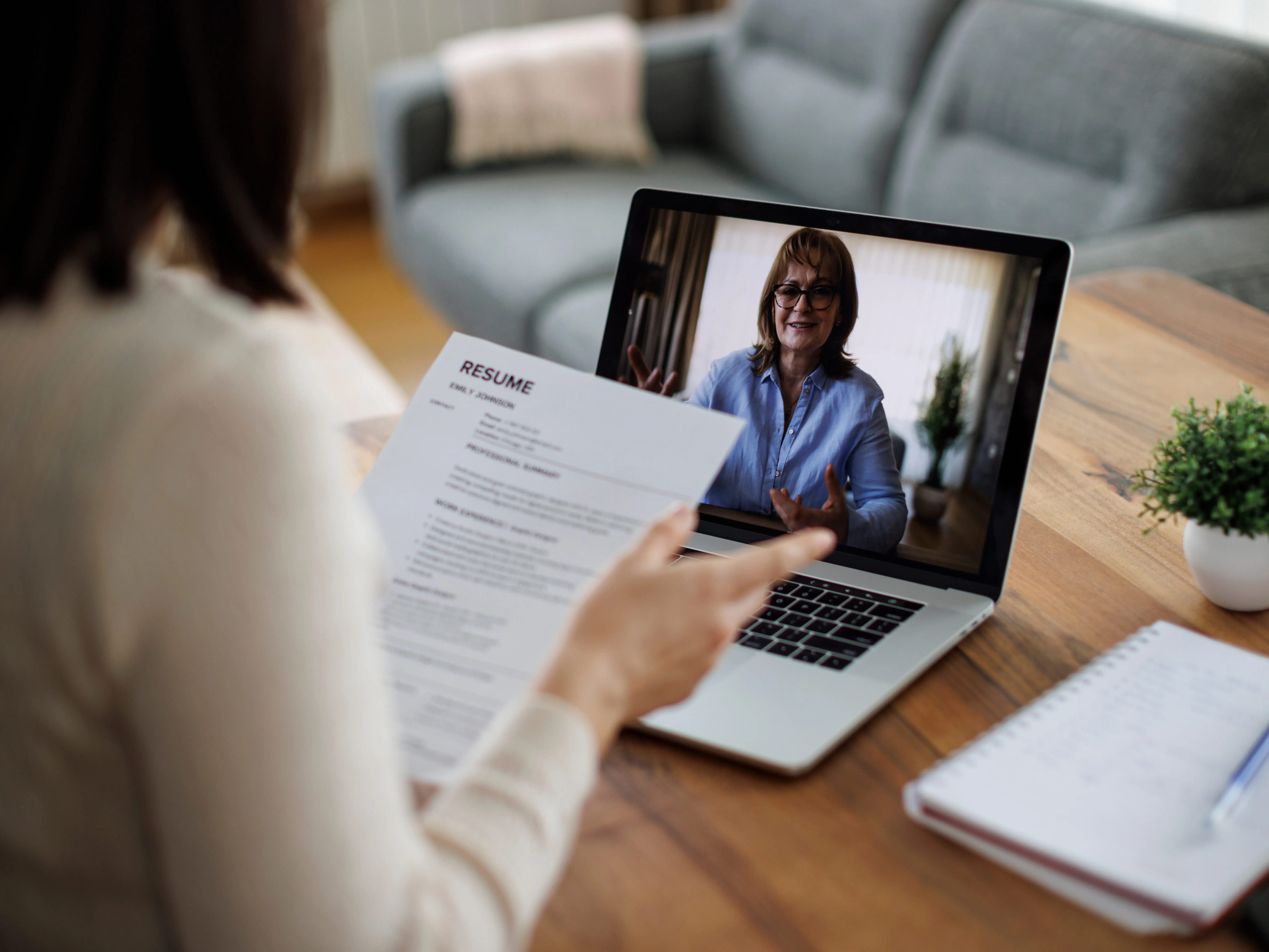A person holds a resume during a video interview on a laptop at a wooden table.