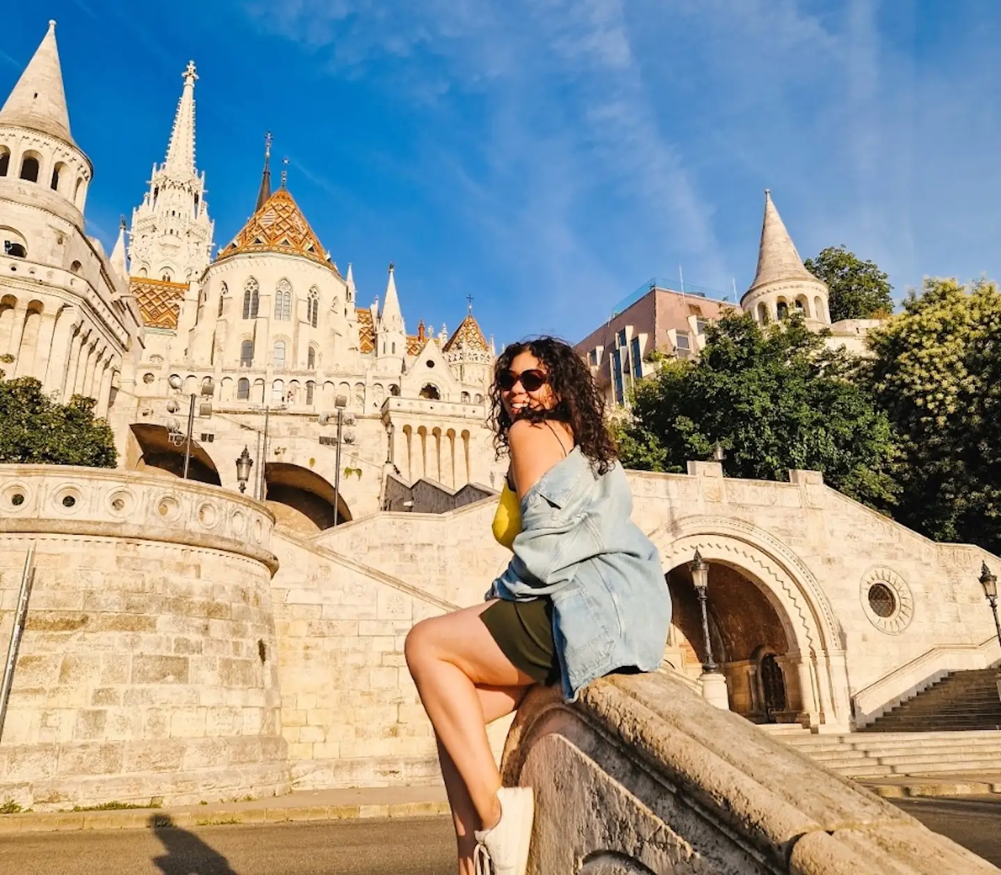 The writer sitting on a ledge at Fisherman's Bastion in Budapest, with buildings in the background.
