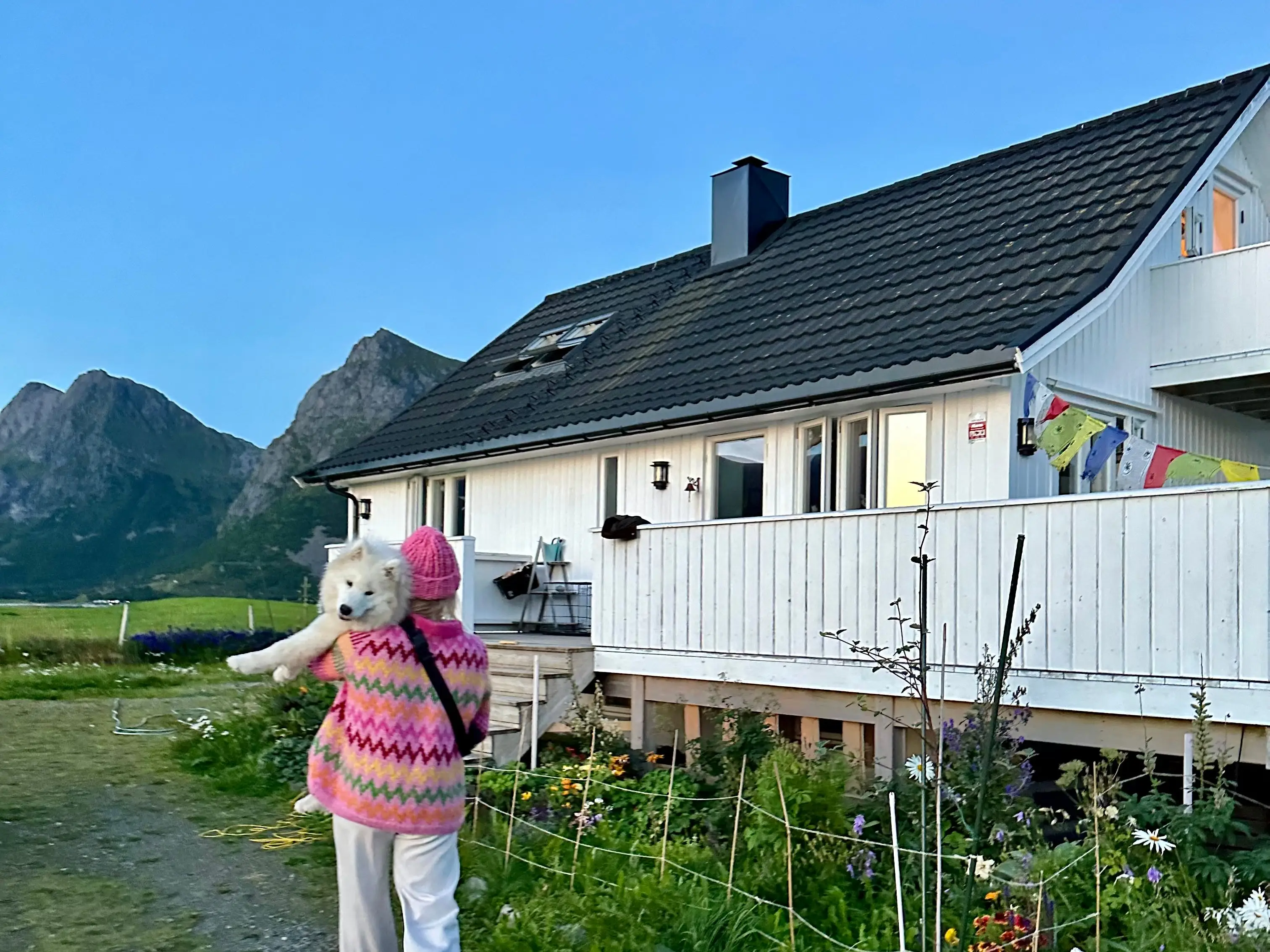 Woman holding dog near House surrounded by mountains, greenery