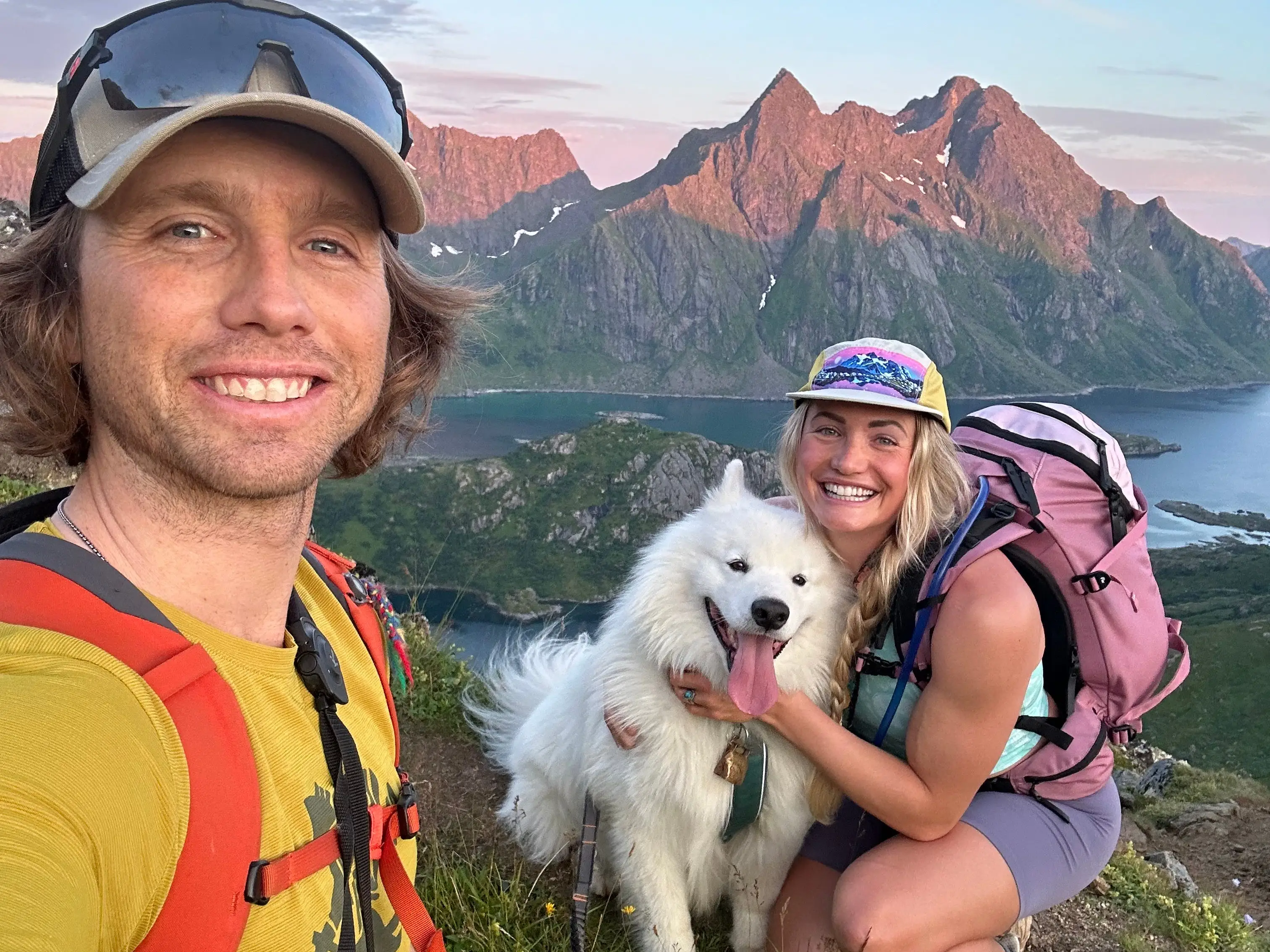 Two people smiling with fluffy white dog in mountains