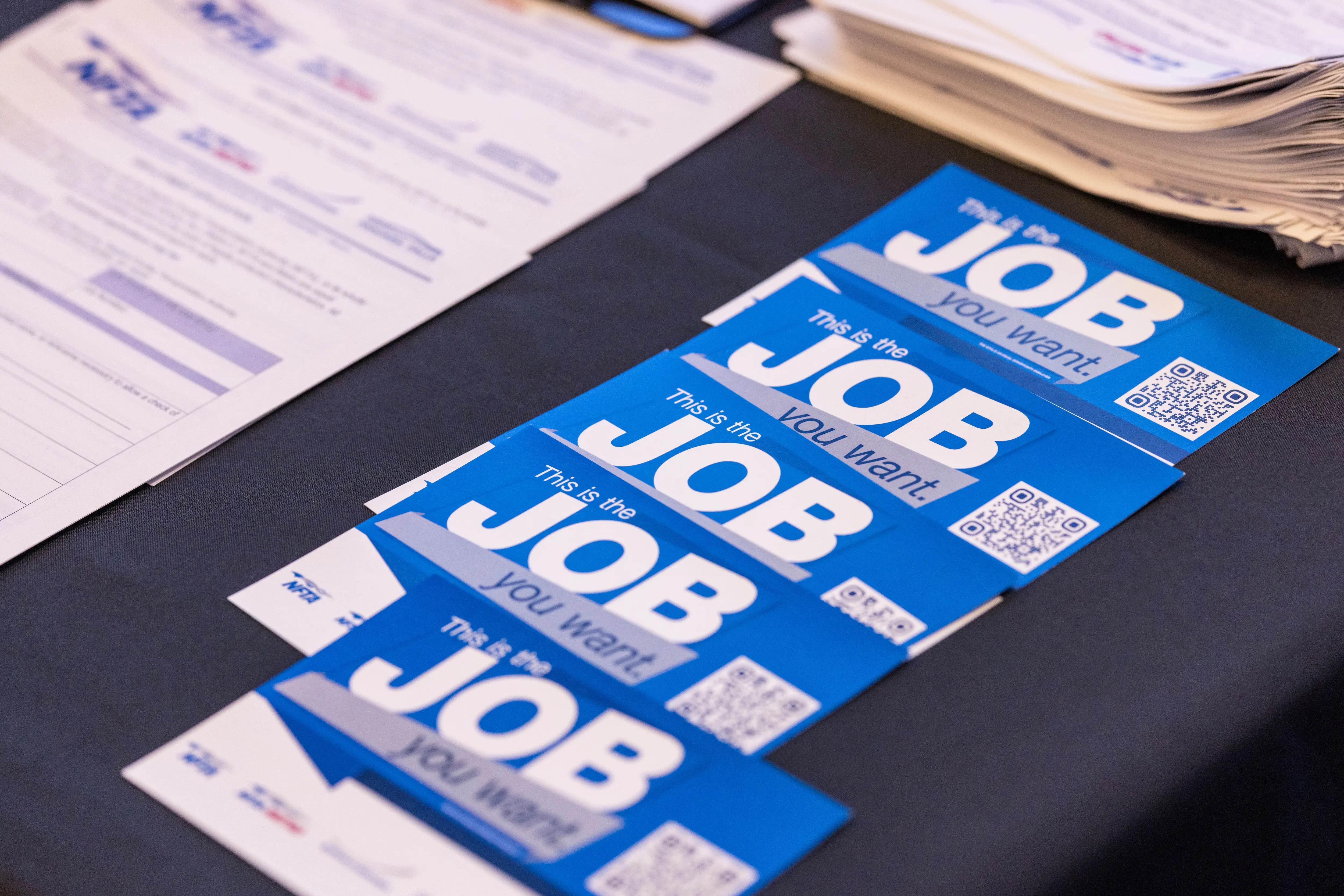 Blue job fair handouts reading “This is the JOB you want.” lie on a table beside paperwork.