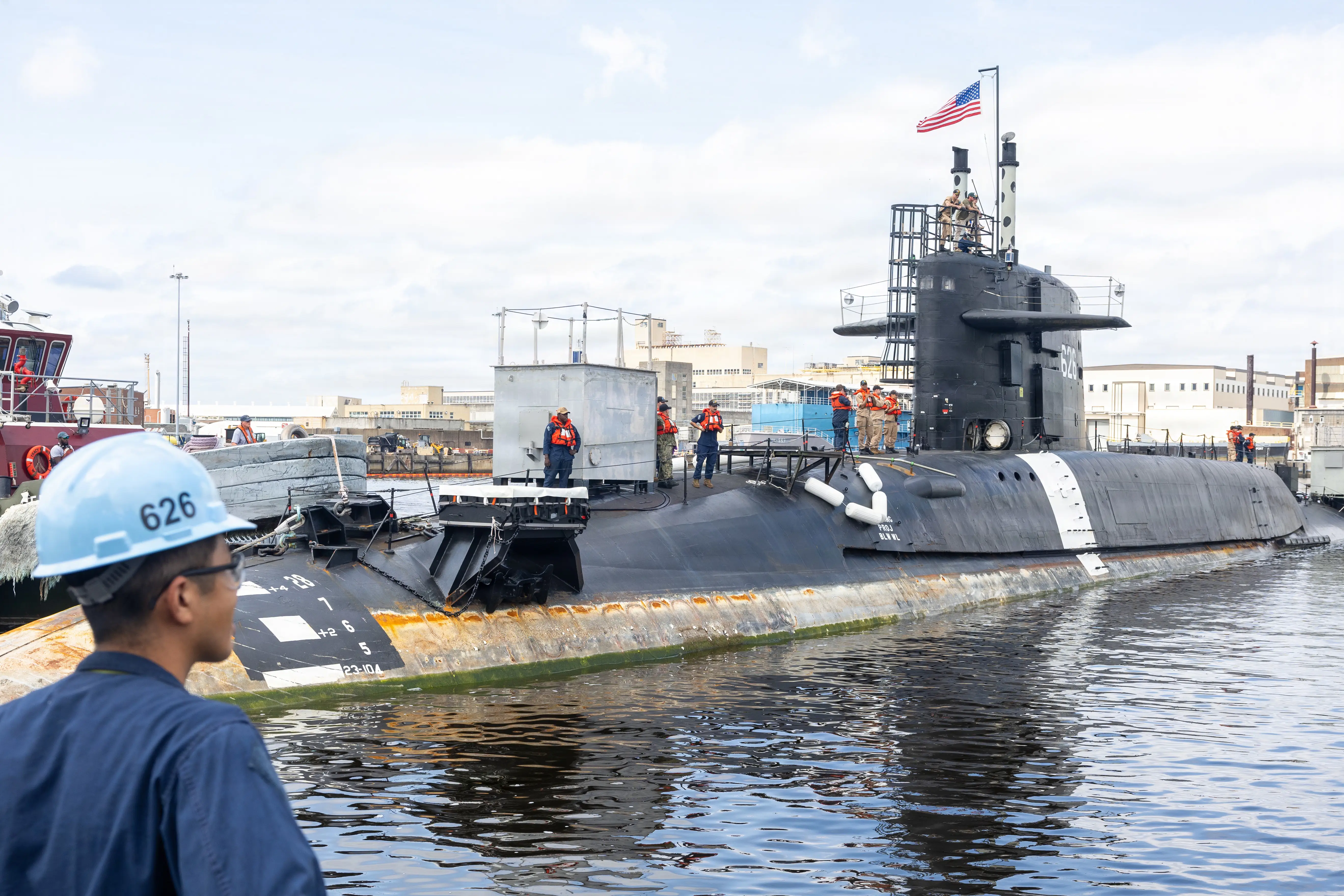 A submarine sits in the water at a shipyard.