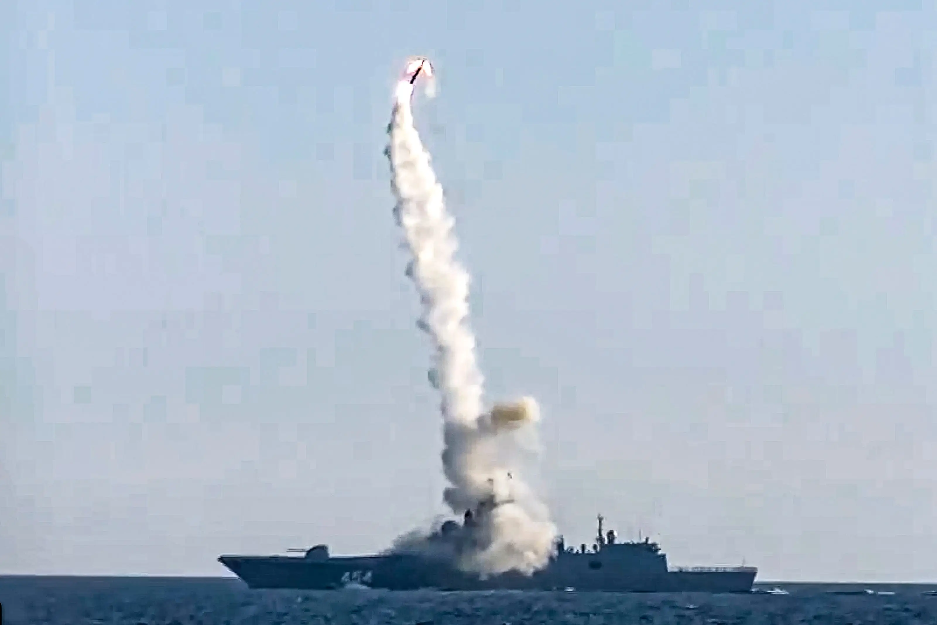 A naval vessel at sea launches a missile, leaving a tall white smoke trail against a pale sky.