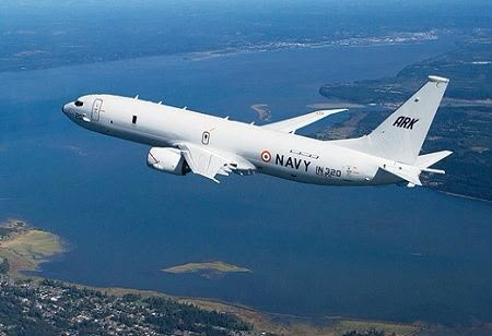 An Indian Navy P8I aircraft flies over a body of water with land visible on either side.