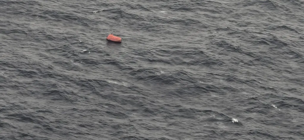 An orange liferaft floating in choppy gray ocean water.