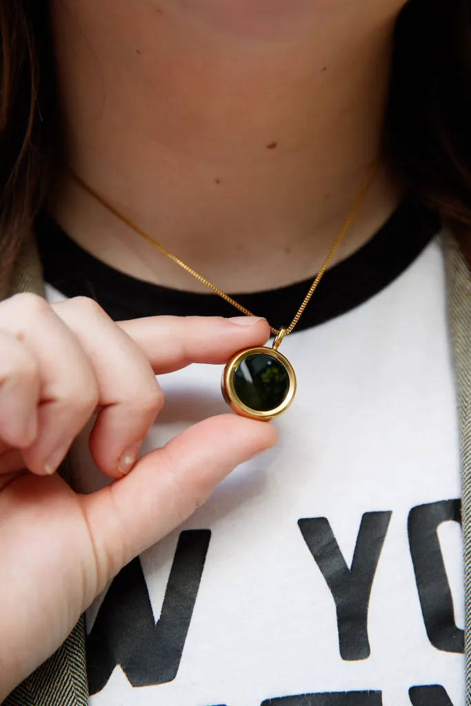 Close-up of McKenzie holding the circular gold UV necklace from Own Your Light.