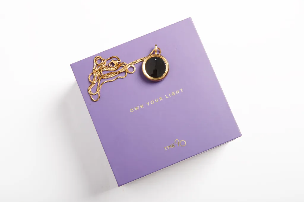 A gold UV necklace from Own Your Light on a purple box.